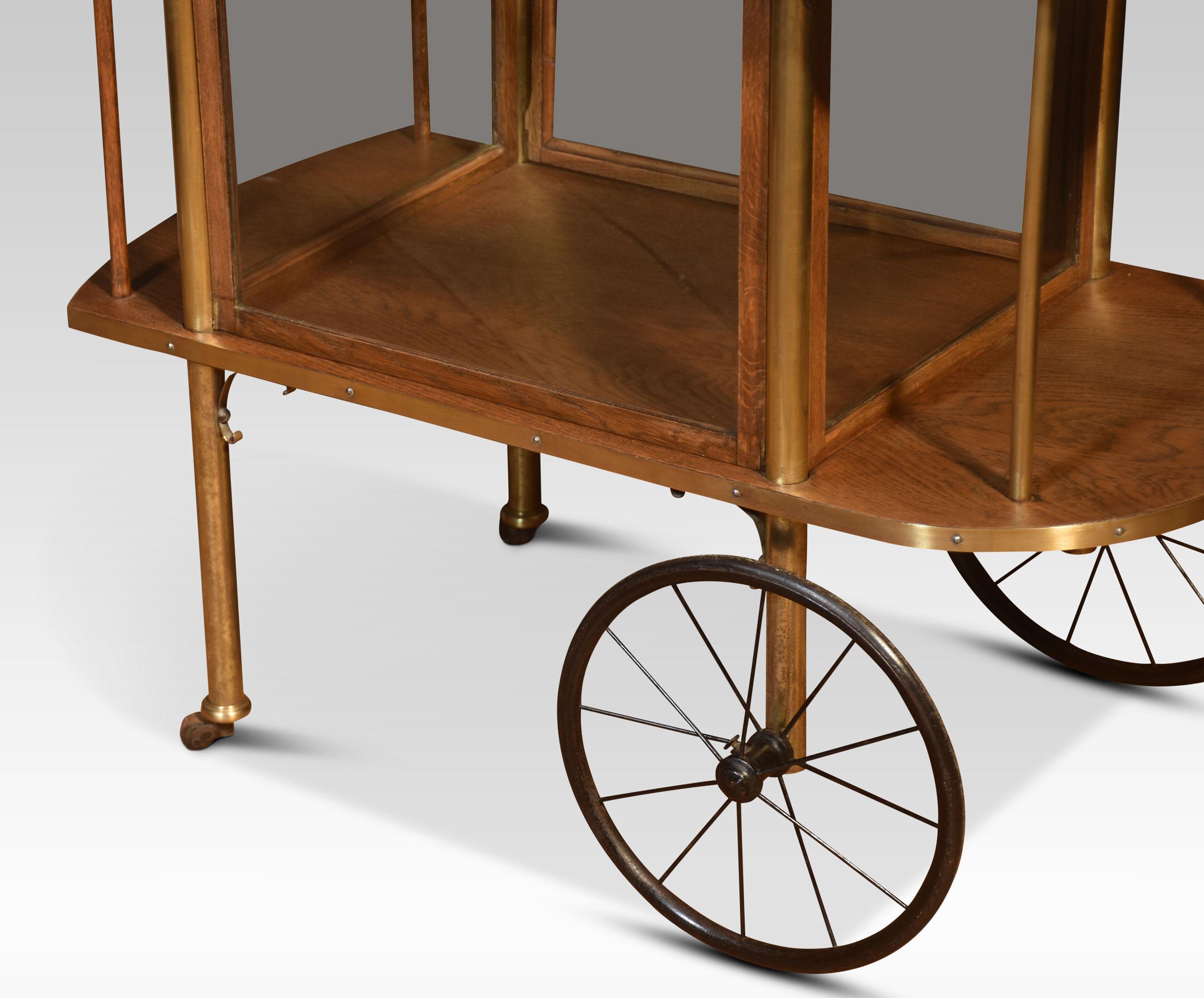 Oak drinks trolly having raised pierced brass gallery to the oak top with inset glass panel. Above large drinks cabinet with glass pannels having drop-down doors. All raised up on circular brass supports terminating in large spoked