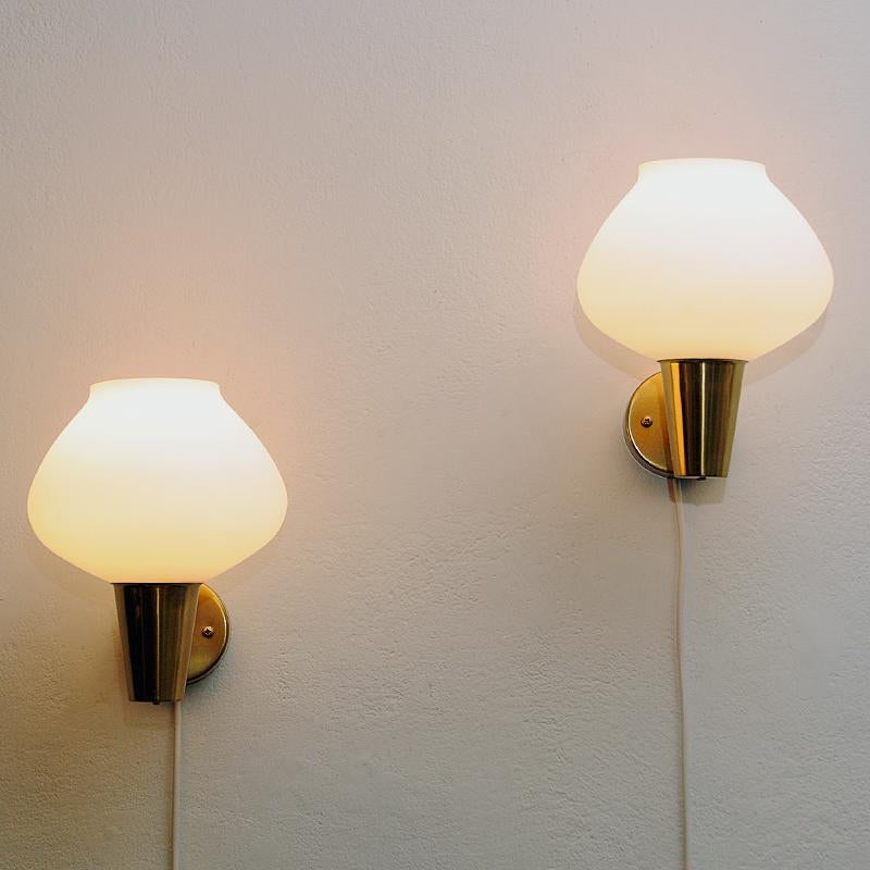 Lovely frosted opaline glass pair of wall lamps made by Asea Sweden 1950s. These classic wall lamps have an oval shaped shade resting on a brass coneshaped cup attached to a brasspole. Great as a pair or even as single lamp in the hallway, bedroom,