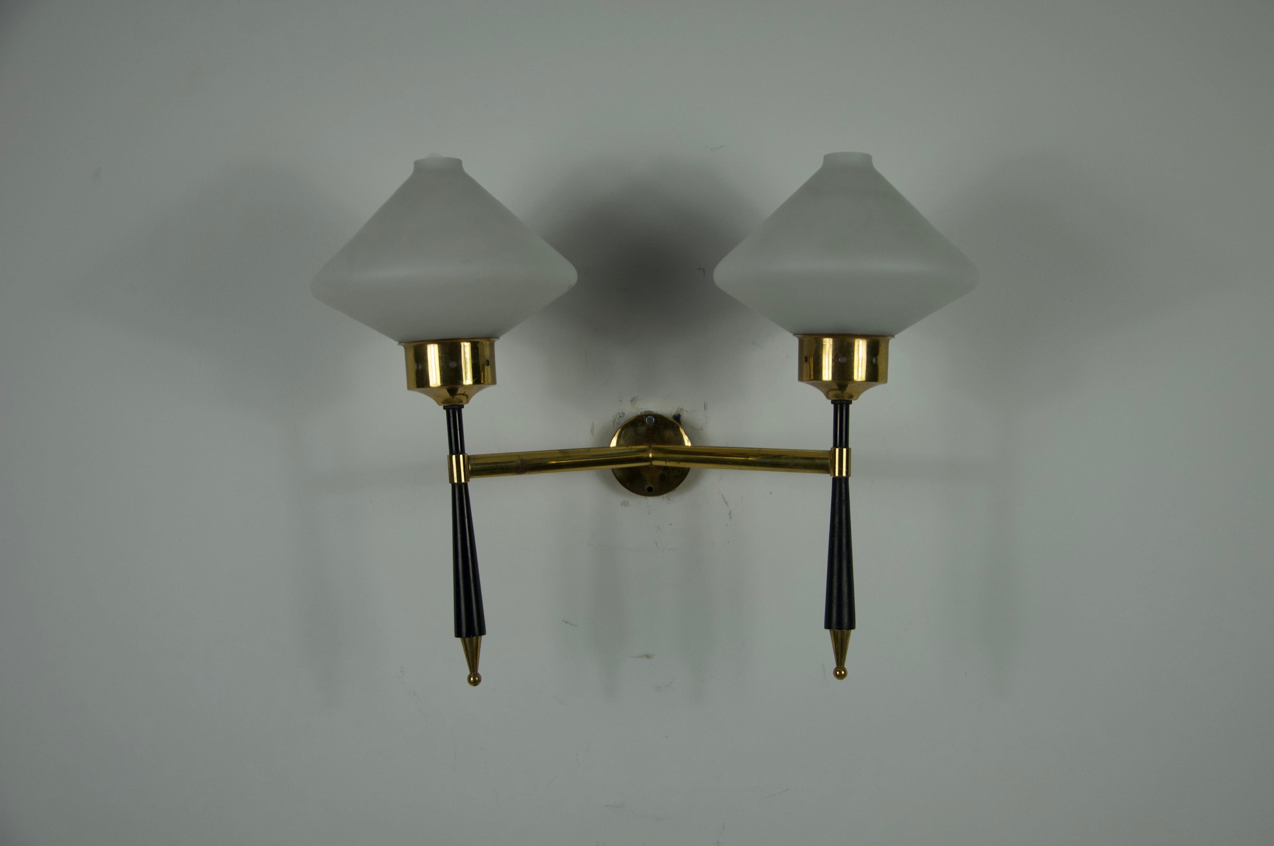Questa elegante lampada da parete è stata progettata e prodotta da Stilnovo in Italia negli anni Sessanta. Caratterizzato da una raffinata combinazione di ottone, metallo laccato nero e paralumi in vetro opalino, questo pezzo incarna la raffinatezza