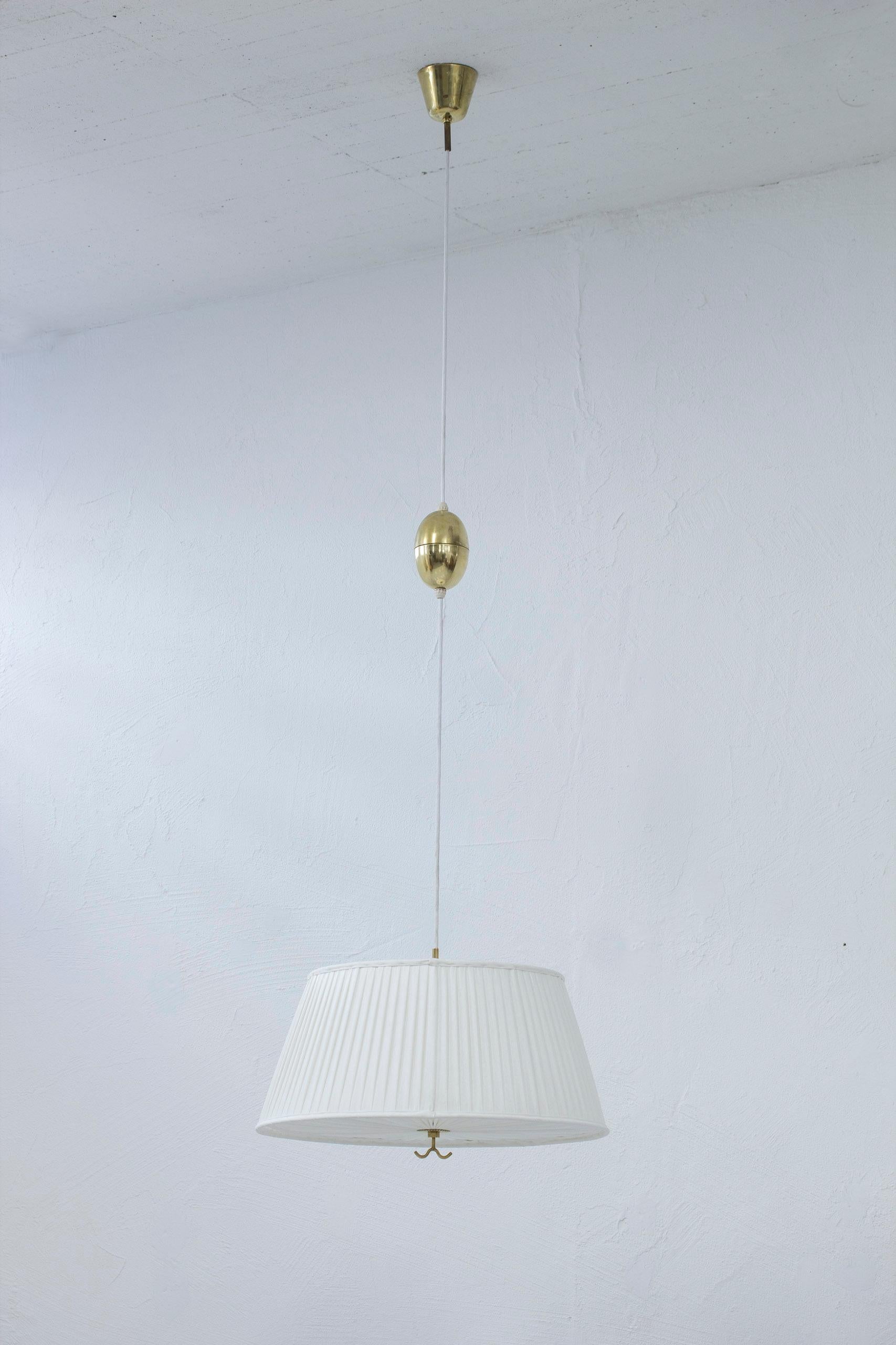 Ceiling lamp model 11558 designed by Harald Notini. Produced in Sweden by Böhlmarks during the 1940s. Ceiling mount, pulley and handle made from brass and shade in hand sewn pleated chintz fabric. The lamp shade has been re-sewn with new fabric and
