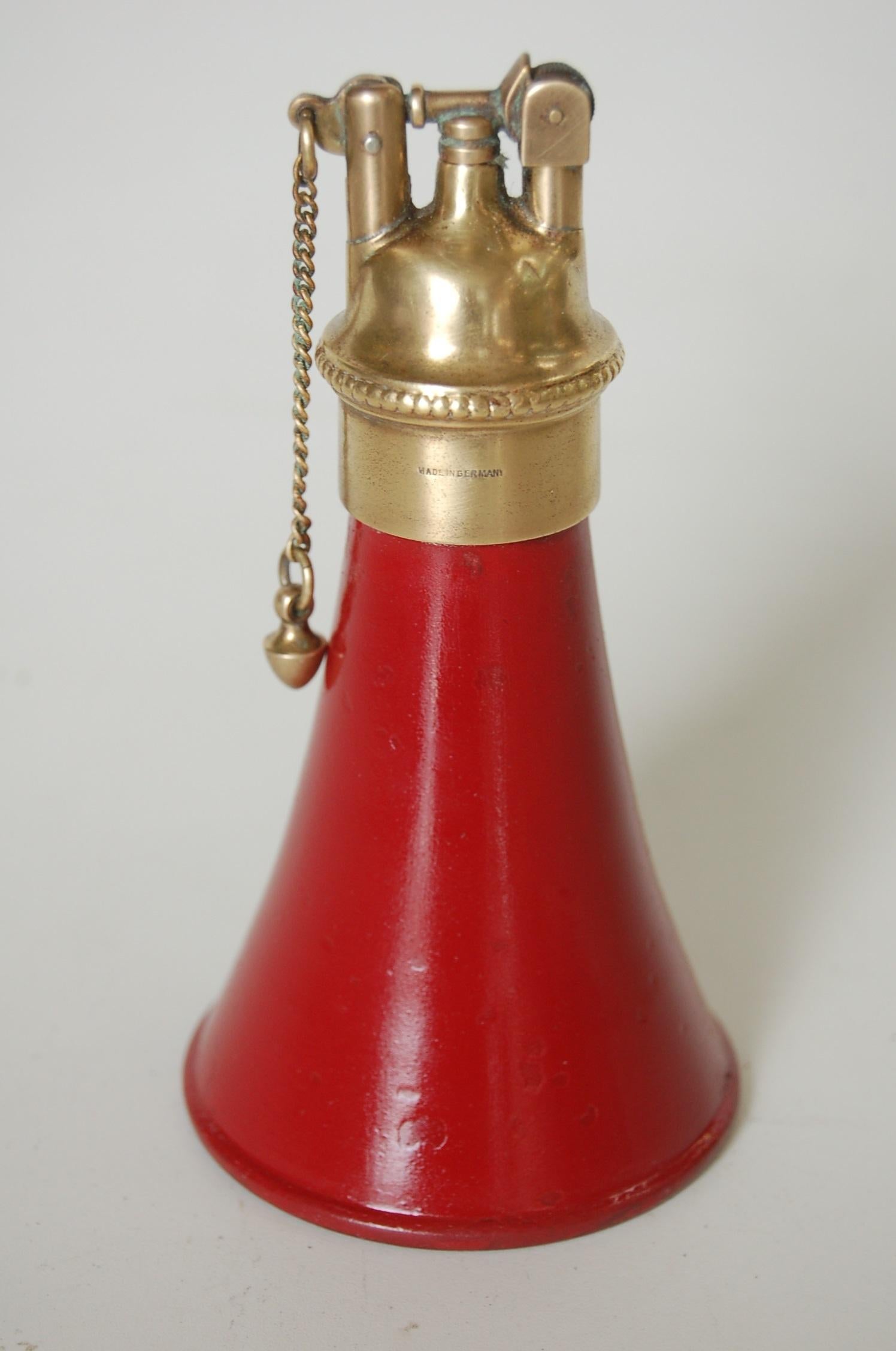 Benzinfeuerzeug aus Messing und rotem Horn in Form eines Tischfeuerzeugs mit Zugkette, hergestellt in Deutschland.

Maße: 5.5