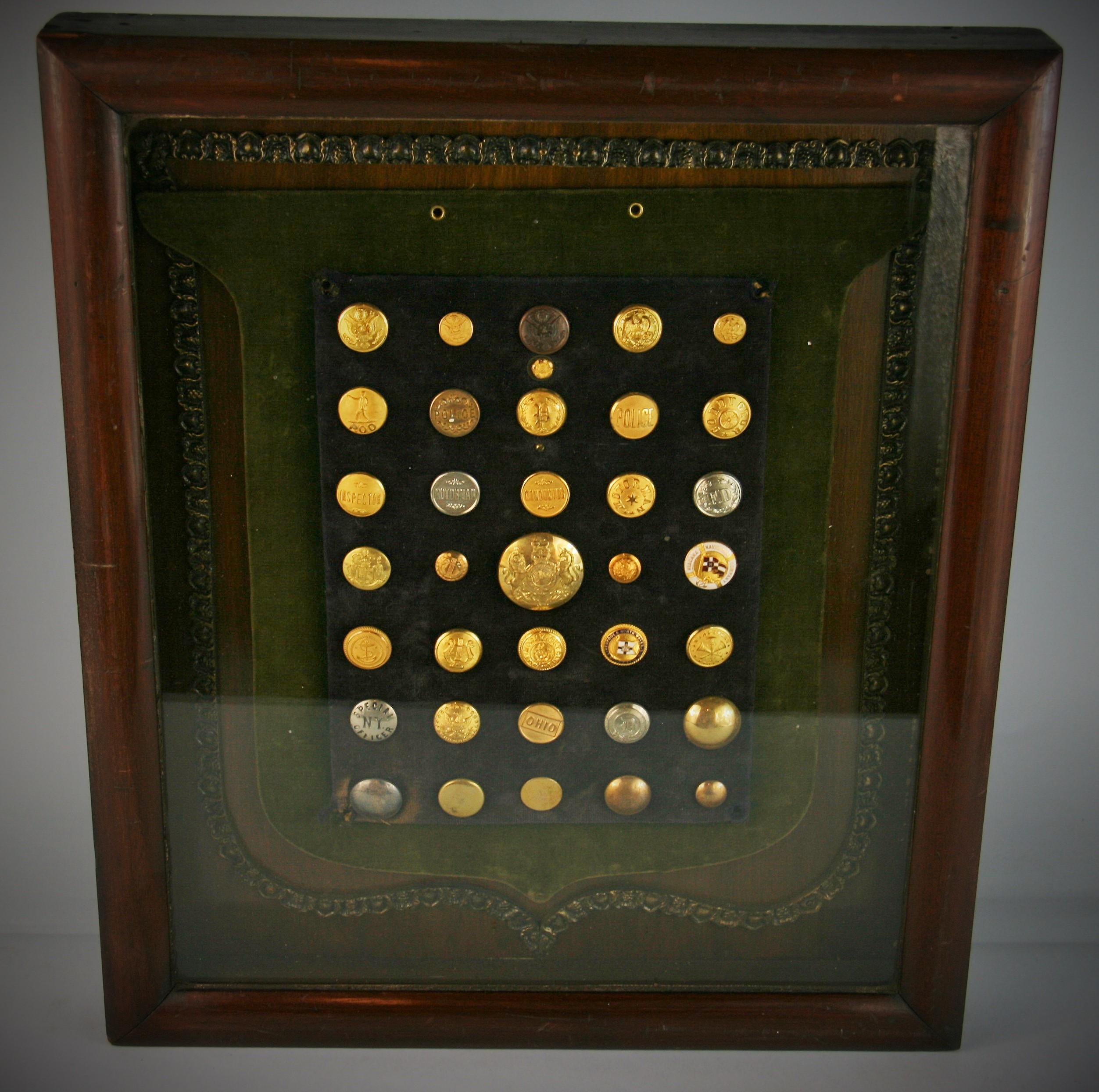 3-642 brass and silver button collection encased in a wood frame set on a green velvet board.