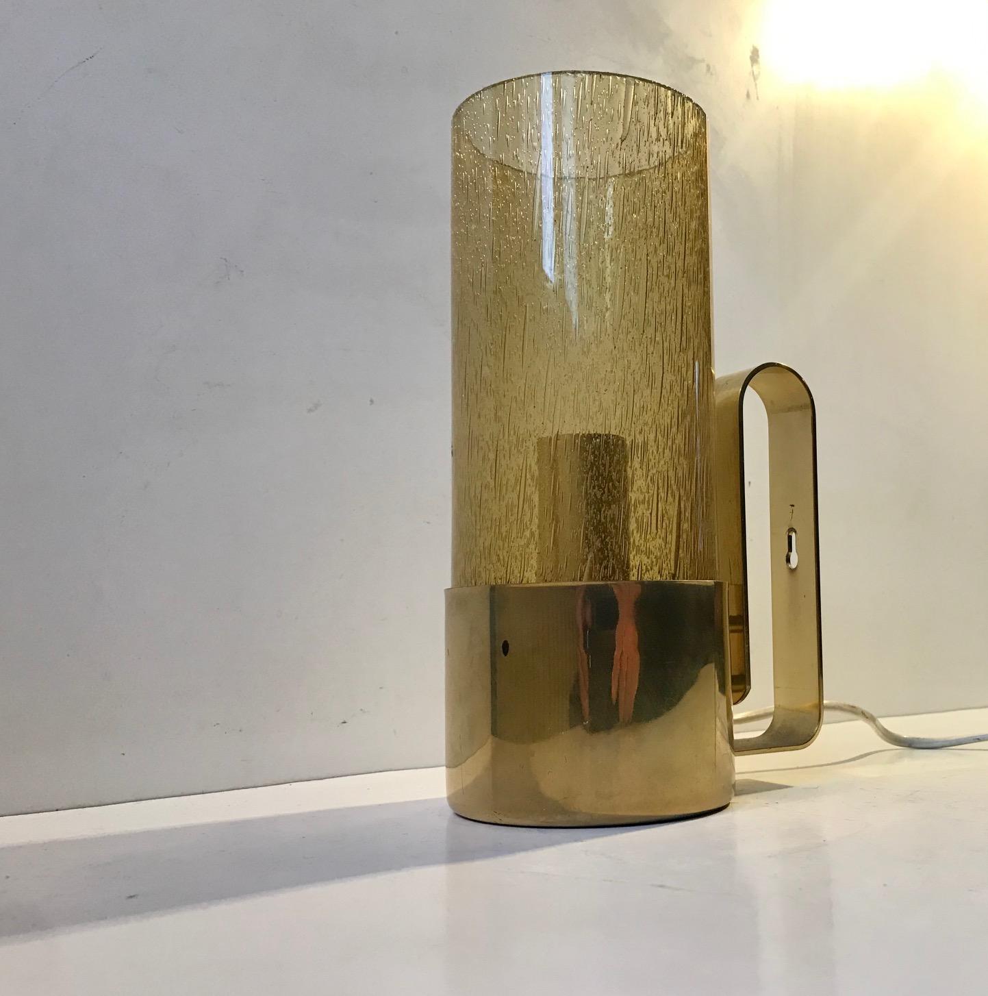 A small (Measure: H 22cm) practical table light made from brass and smoked blister glass. Designed and manufactured by Nya Ôia in Sweden during the late 1960s or early 70s. It can also be hung as a wall lamp.