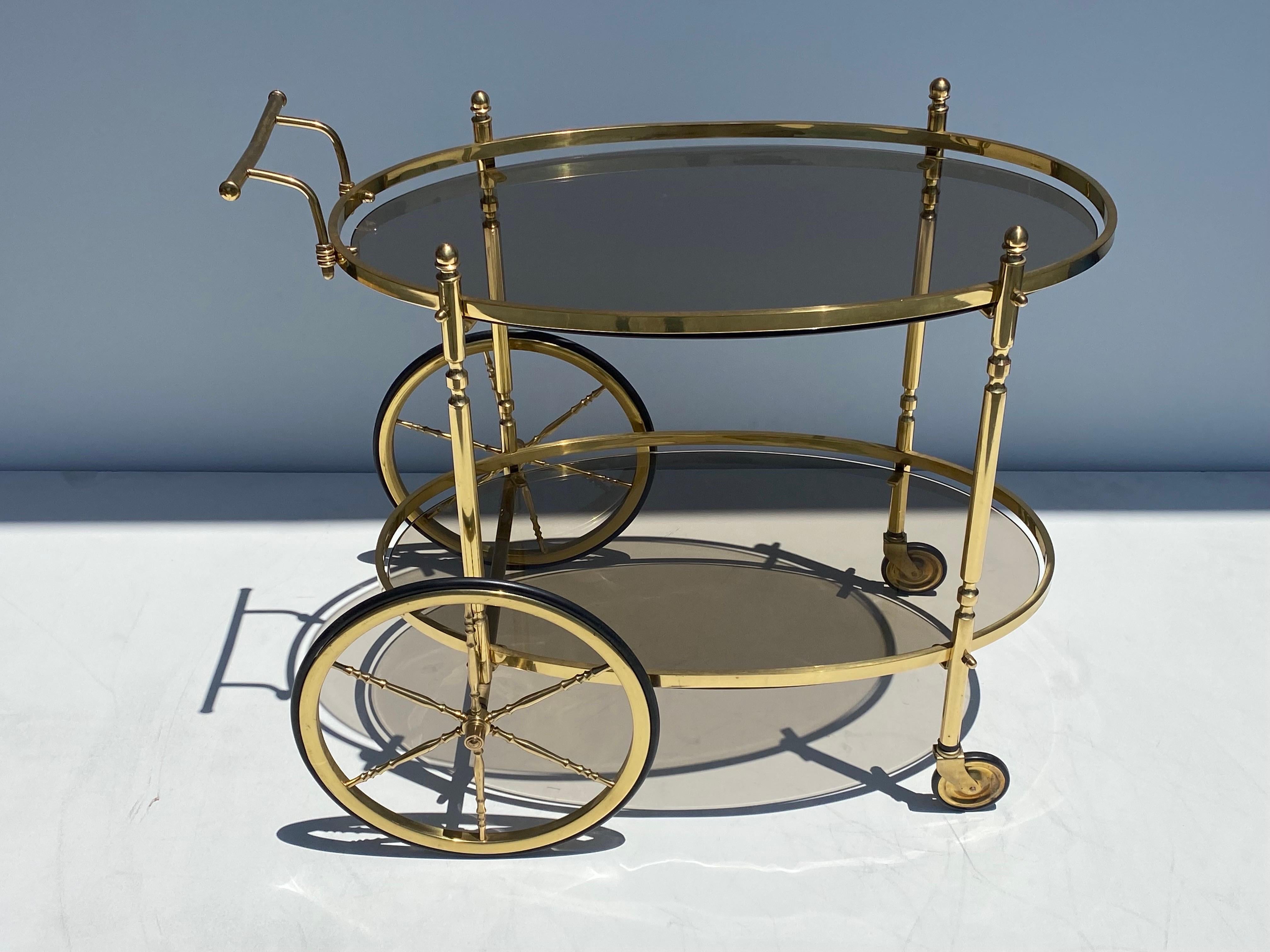 Brass and smoked glass two tired oval serving bar cart with beautiful large wheels. There is a 1/4