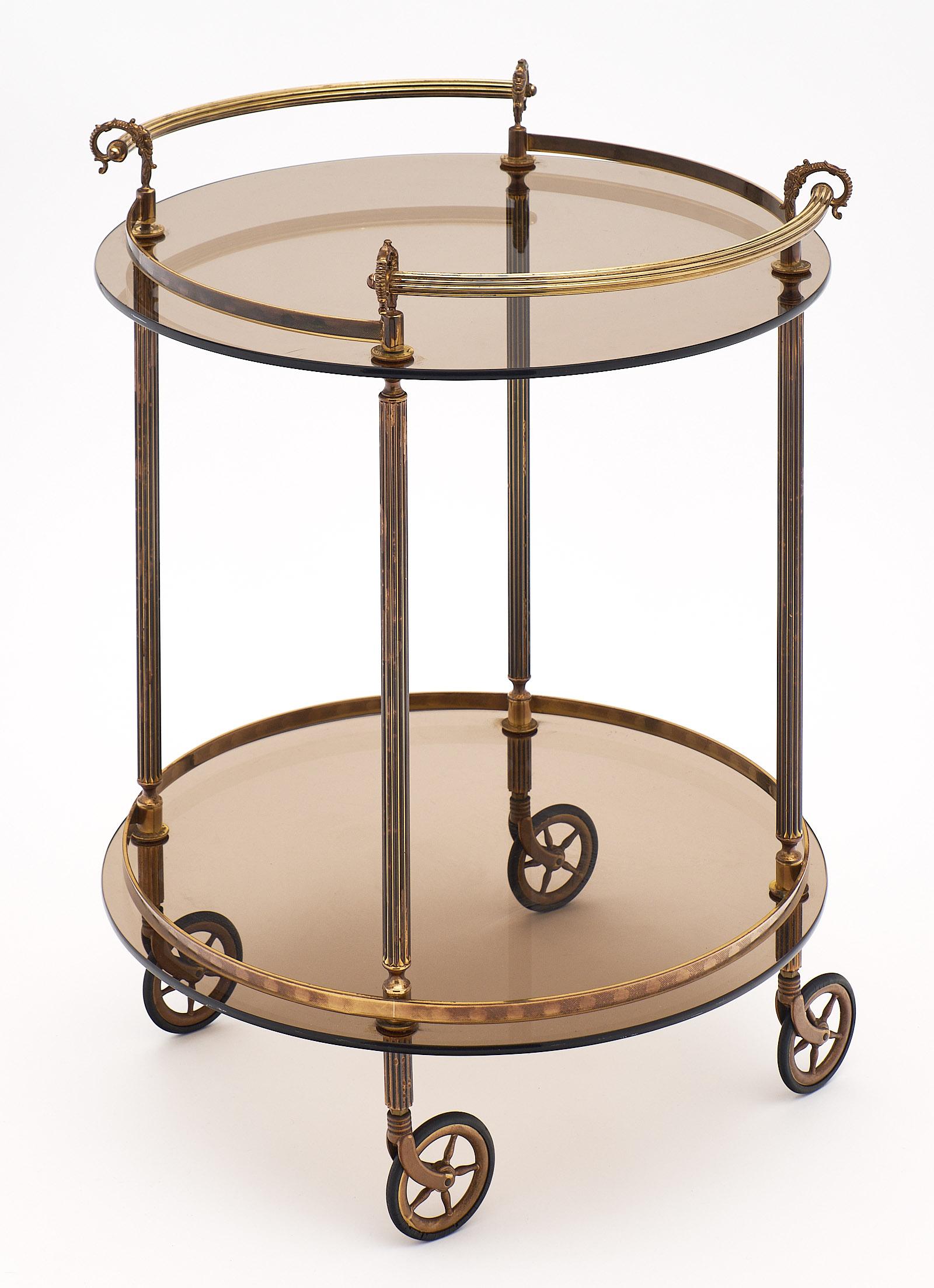 Chariot de bar français en laiton et verre fumé avec deux poignées et roues d'origine. Cette pièce a une structure en laiton avec des détails incurvés. Il y a deux niveaux de verre fumé teinté. Les roues fonctionnent très bien et sont souples. Nous