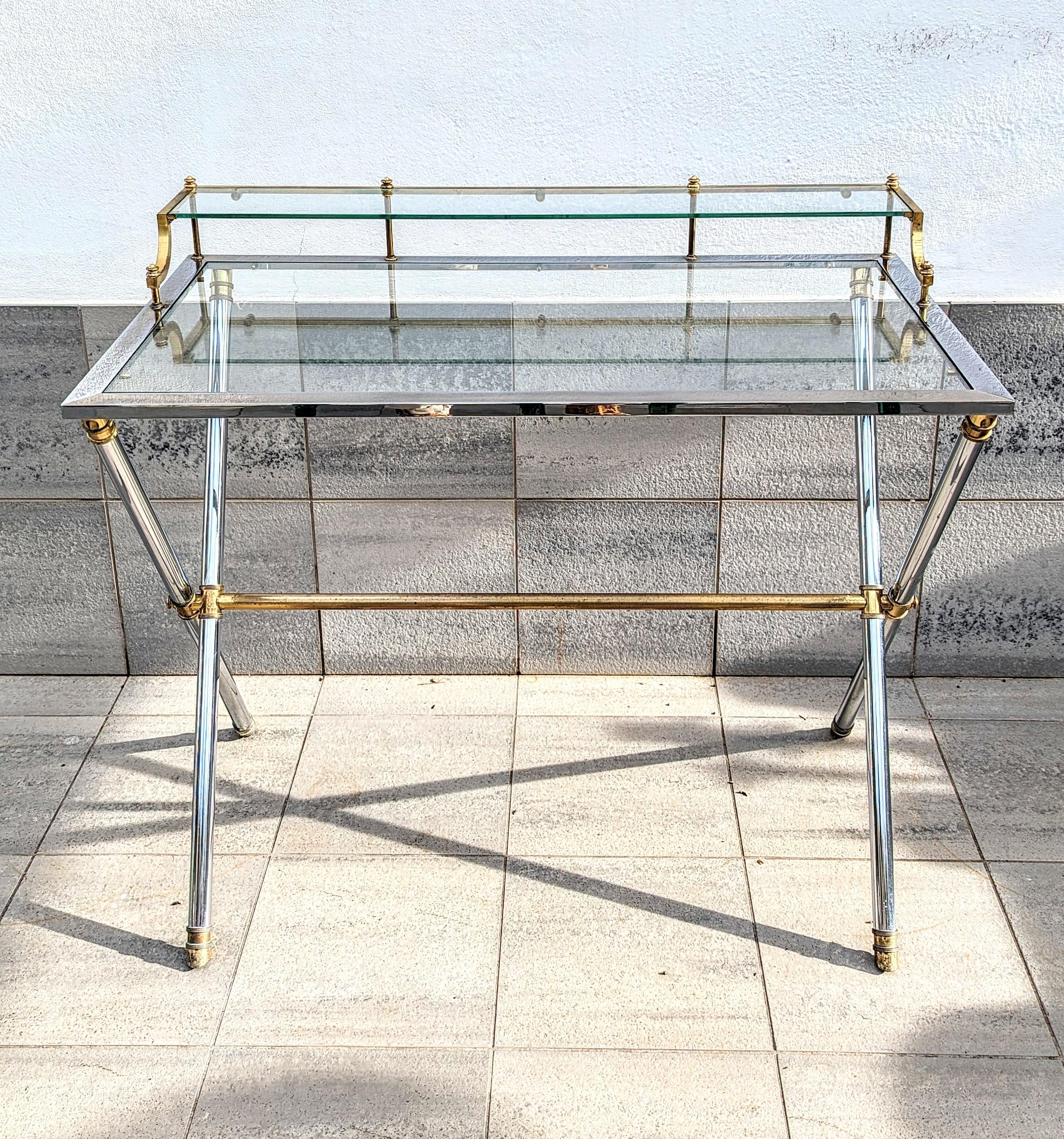Maison Jansen brass and steel desk, silver and gold patina with a rectangular Glass top resting on a cylindrical X-frame base connected by a stretcher. 

Maison Jansen was a Paris-based interior decoration office founded in 1880 by Dutch-born