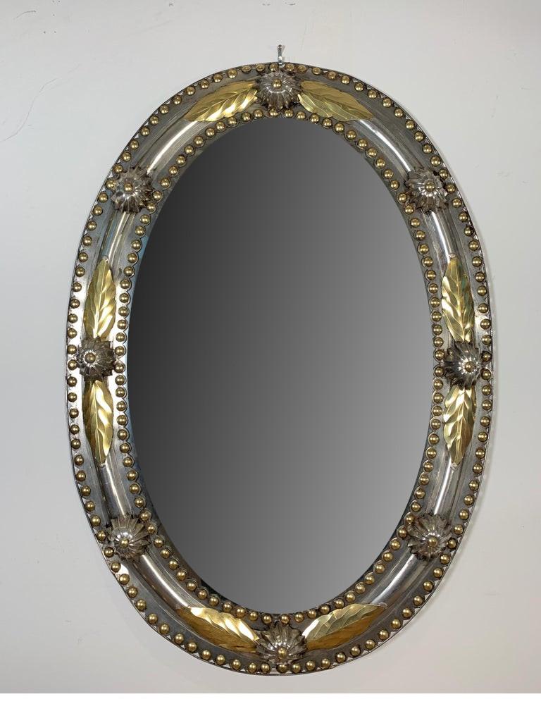 Decorative oval mirror with sheet steel frame with brass accents. The frame is stamped out to have a high relief design but is very lightweight.