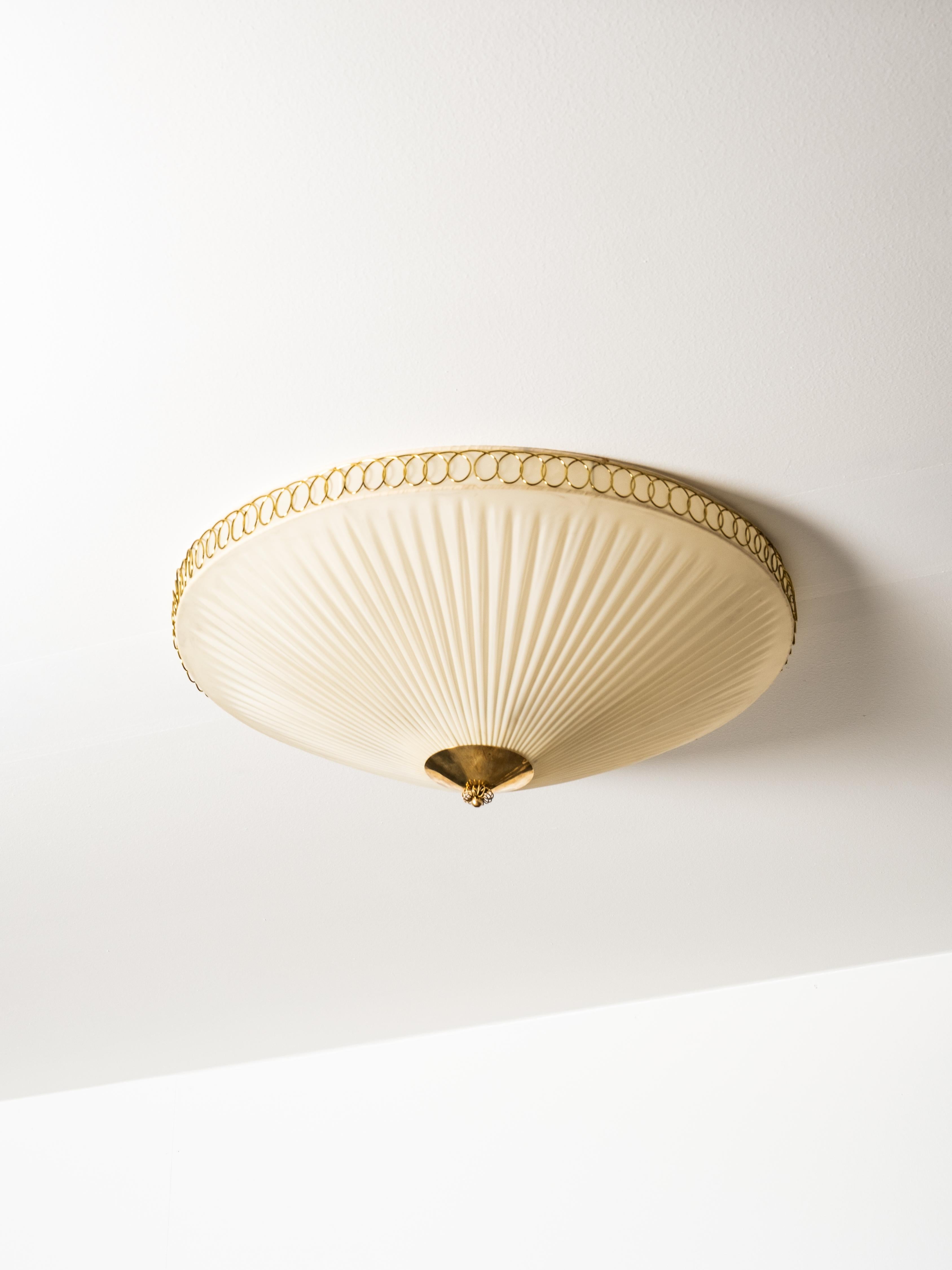 A mid-century flush mount ceiling light by Idman, Finland, from the 1950s. The lamp features a circular brass frame with a finely woven synthetic textile diffuser that softens the light evenly across the surface. The clean geometry and restrained