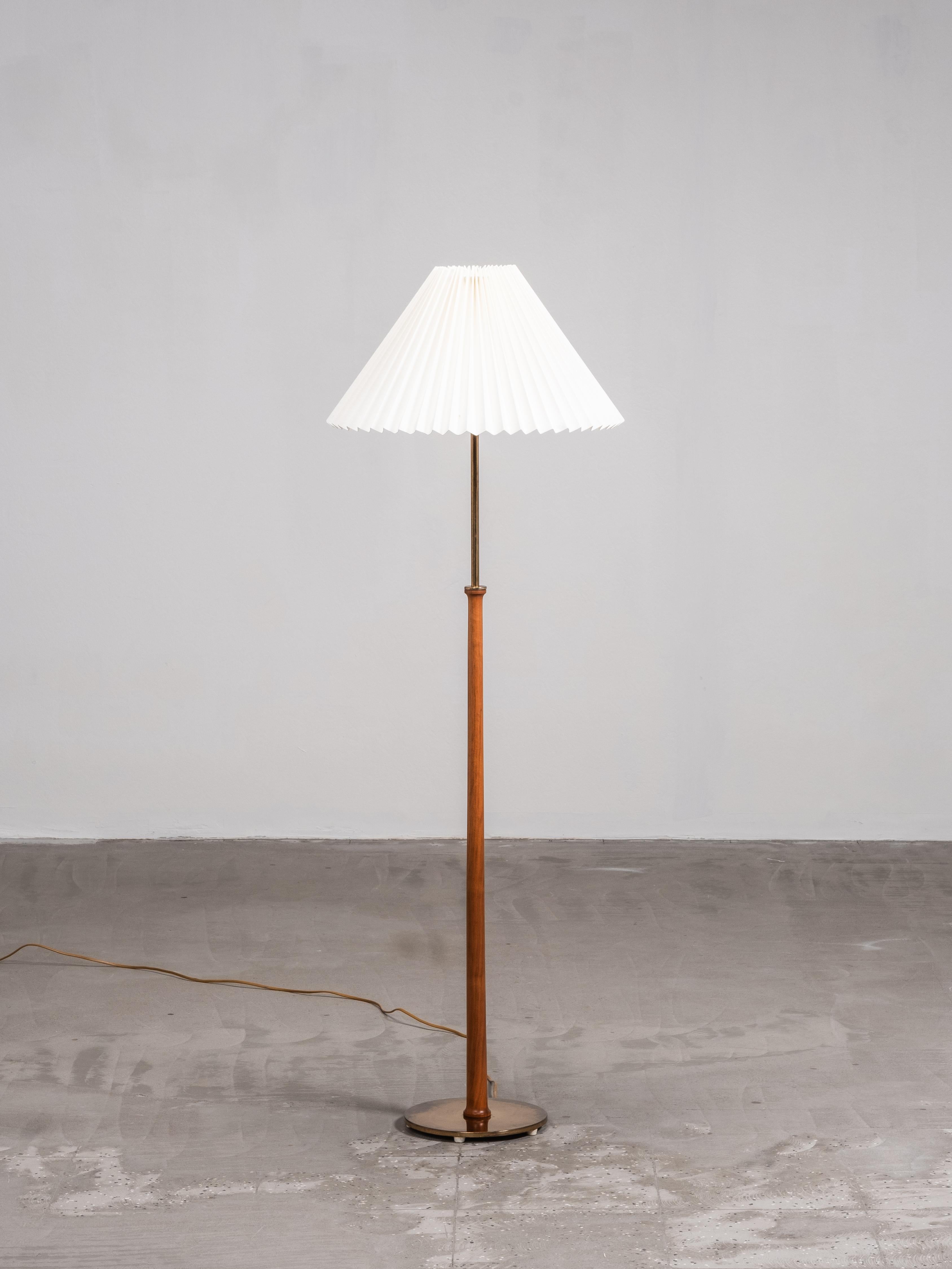 Lampadaire raffiné de Eje Ahlgren pour Bergboms, Suède, modèle G-012. Le design combine une tige en teck massif avec des détails en laiton et une base circulaire en laiton. Son abat-jour en tissu plissé diffuse la lumière de manière homogène, créant