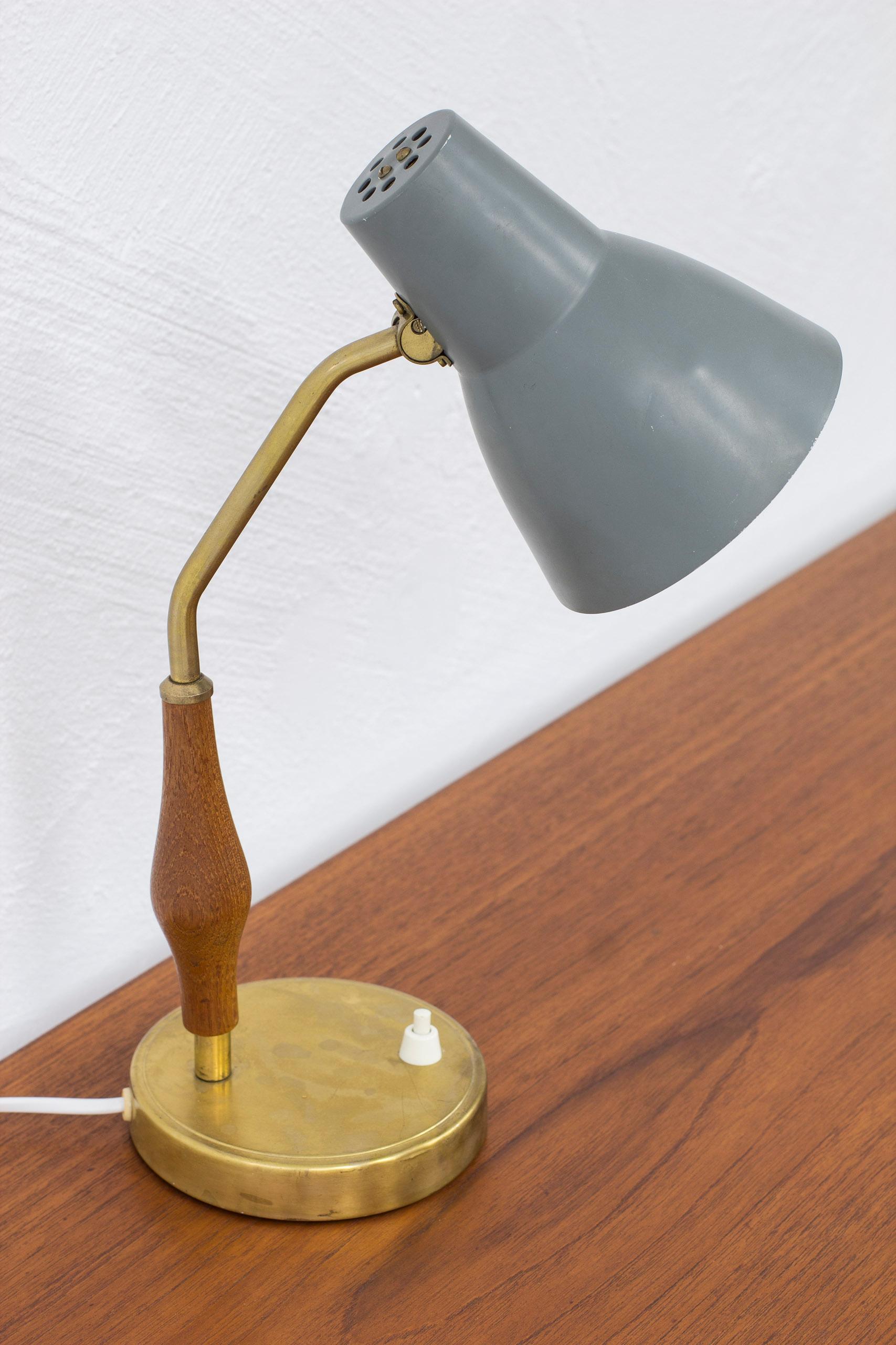 Table lamp produced in Sweden by ASEA belysning. Made sometime during the 1950s. Brass base and stem with solid teak handle and grey and white lacquered aluminum shade. Shade adjustable in angle. Light switch on the lamp base in working order. Good