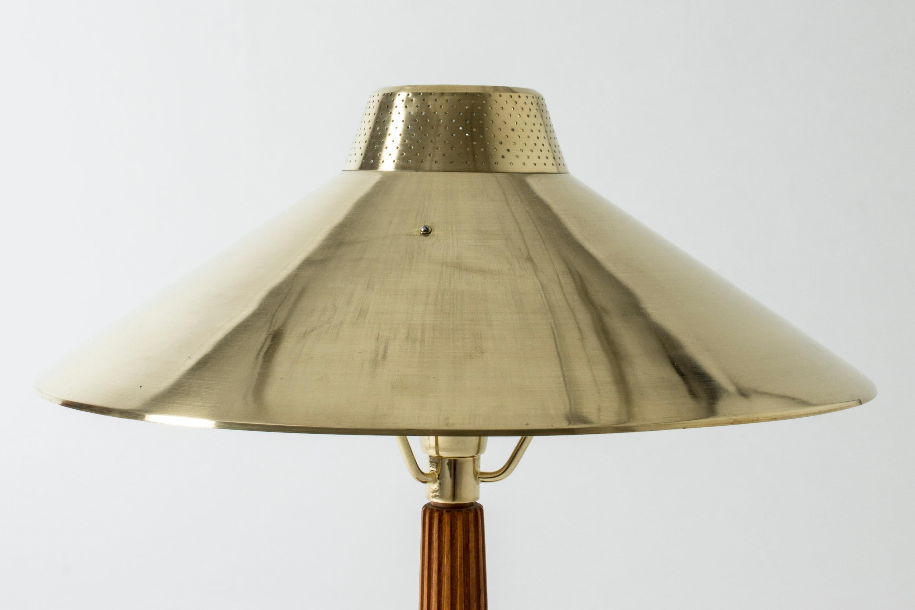 Elegant brass table lamp by Hans Bergström, with a large shade. Shade perforated with tiny holes around the top, creating a warm glow. Mahogany handle with embossed stripes.