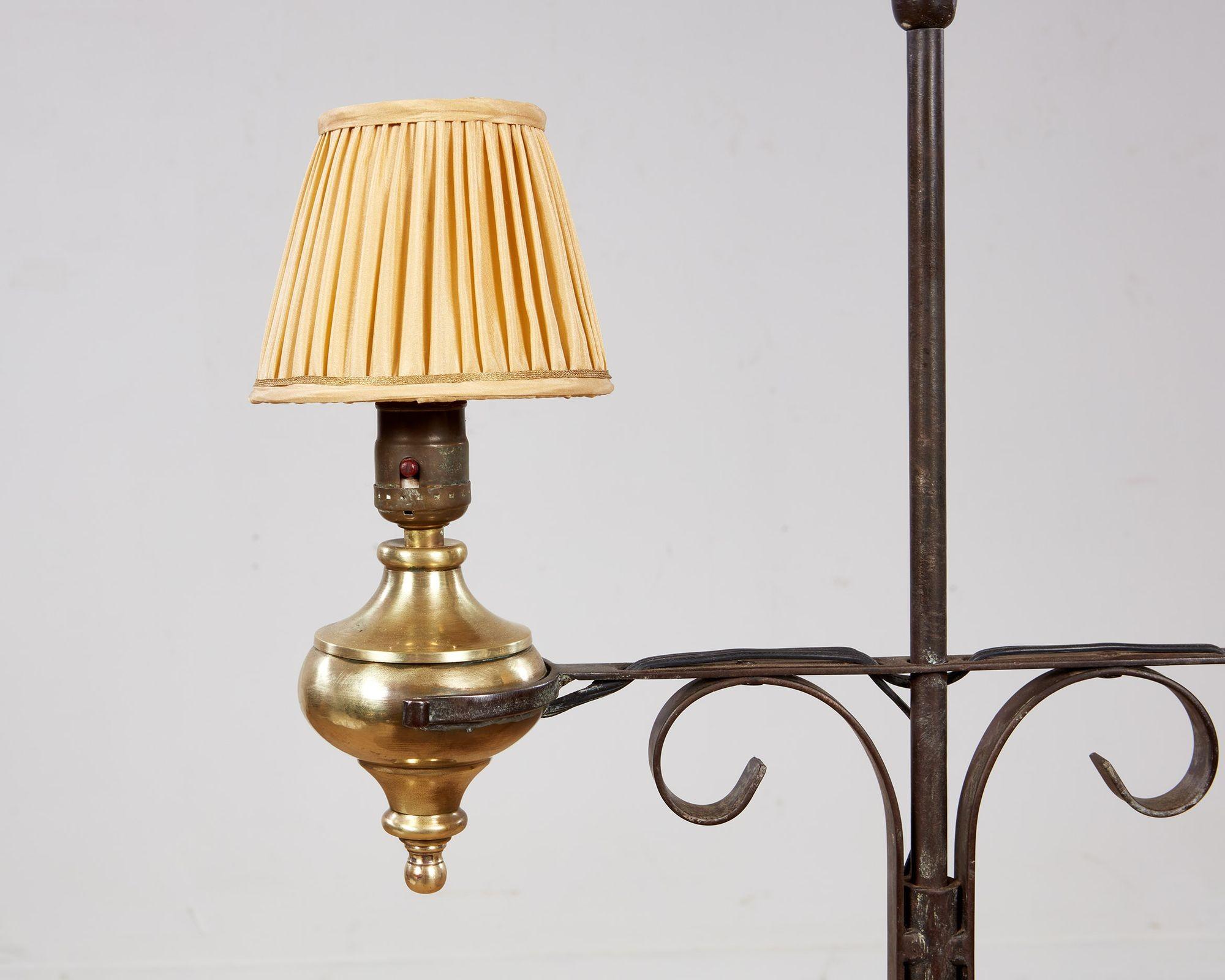 Un lampadaire avec deux urnes en laiton sur une barre transversale réglable en hauteur soutenue par des consoles courbées sur un arbre en fer forgé surmonté d'un fleuron en fer tourné et reposant sur des jambes arquées en tripode avec une monture