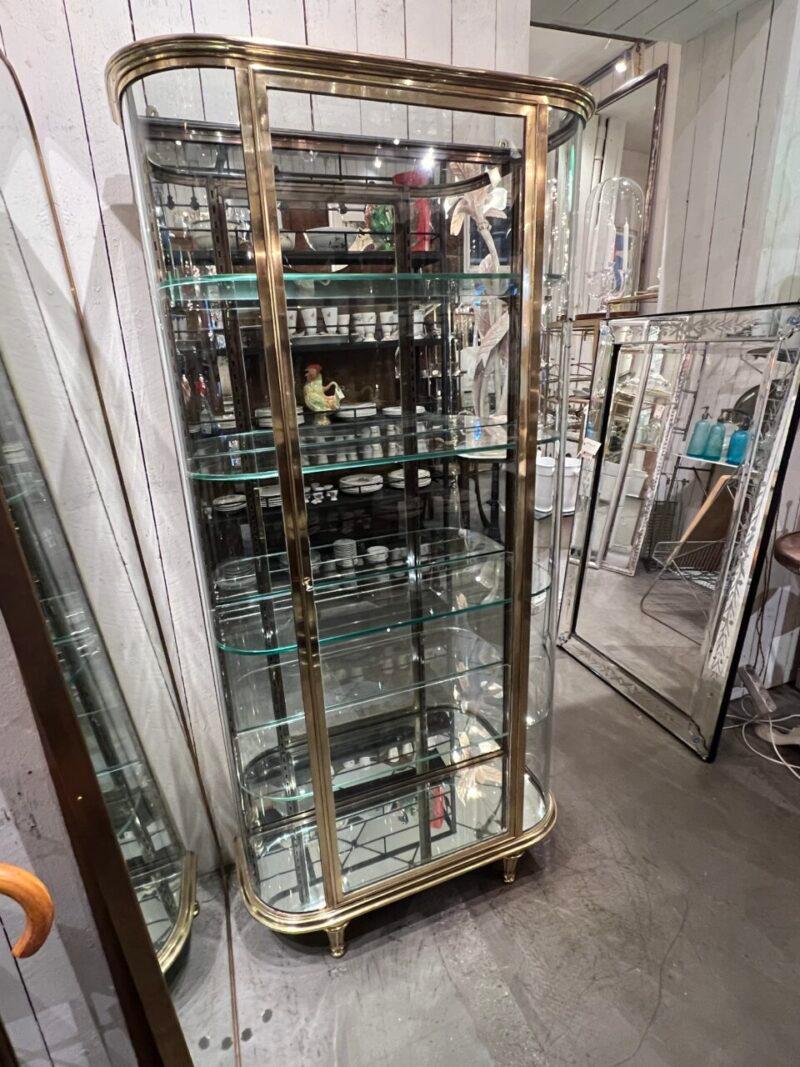 A very elegant display cabinet with delectable curved glass corners, this is a French 1930s stringent  Art Deco style vitrine, with sleek and rigorous profiles and channeled legs.

Formed in quality brass with 4 thick glass shelves and adjustable
