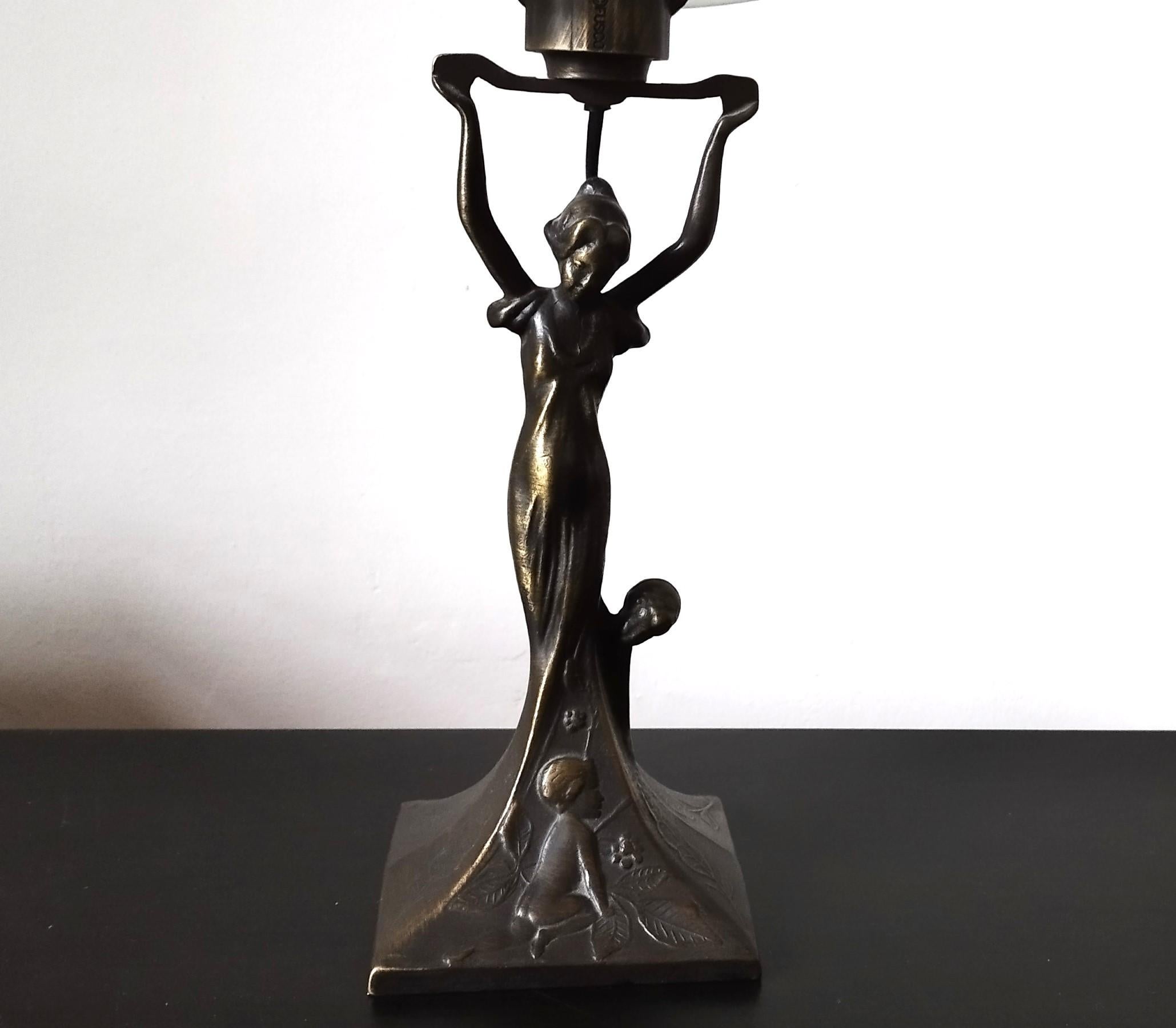 Lampe de table Art déco avec un motif de mère et d'enfant. Le corps massif en laiton présente une patine attrayante. L'abat-jour en verre glacé est en très bon état. La lampe fonctionne parfaitement.