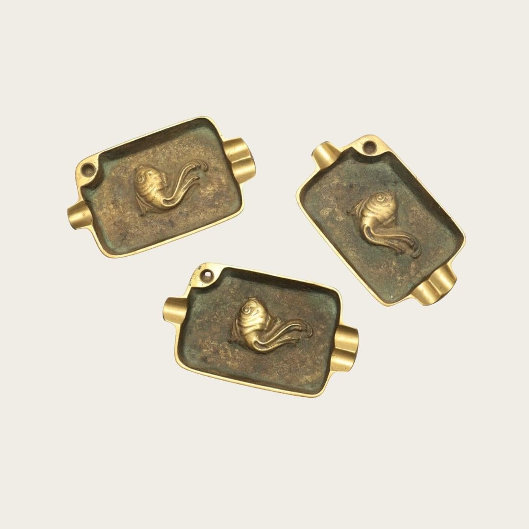 1940er Jahre, Schweden. Trio von Messing-Aschenbechern mit handgegossenen Fischreliefs und skulpturalen Ablagen. Anonymes Werk eines Herstellers, das für Sammler skandinavischer Metallarbeiten aus der Mitte des Jahrhunderts eine besondere