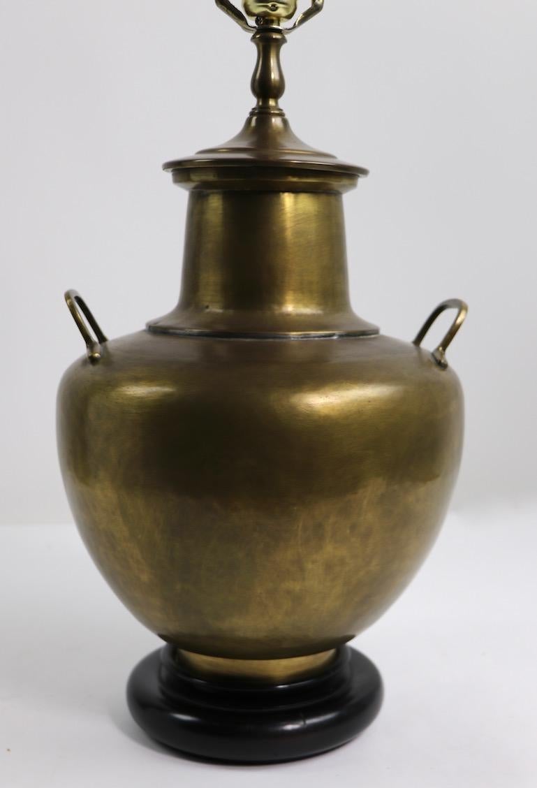 Brass urn or jug form table lamp, mounted on black lacquered plinth base. This example is in very Fine, original and working condition. The brass body has a minor crease in the rear of the lamp, inconsequential, and consistent with age