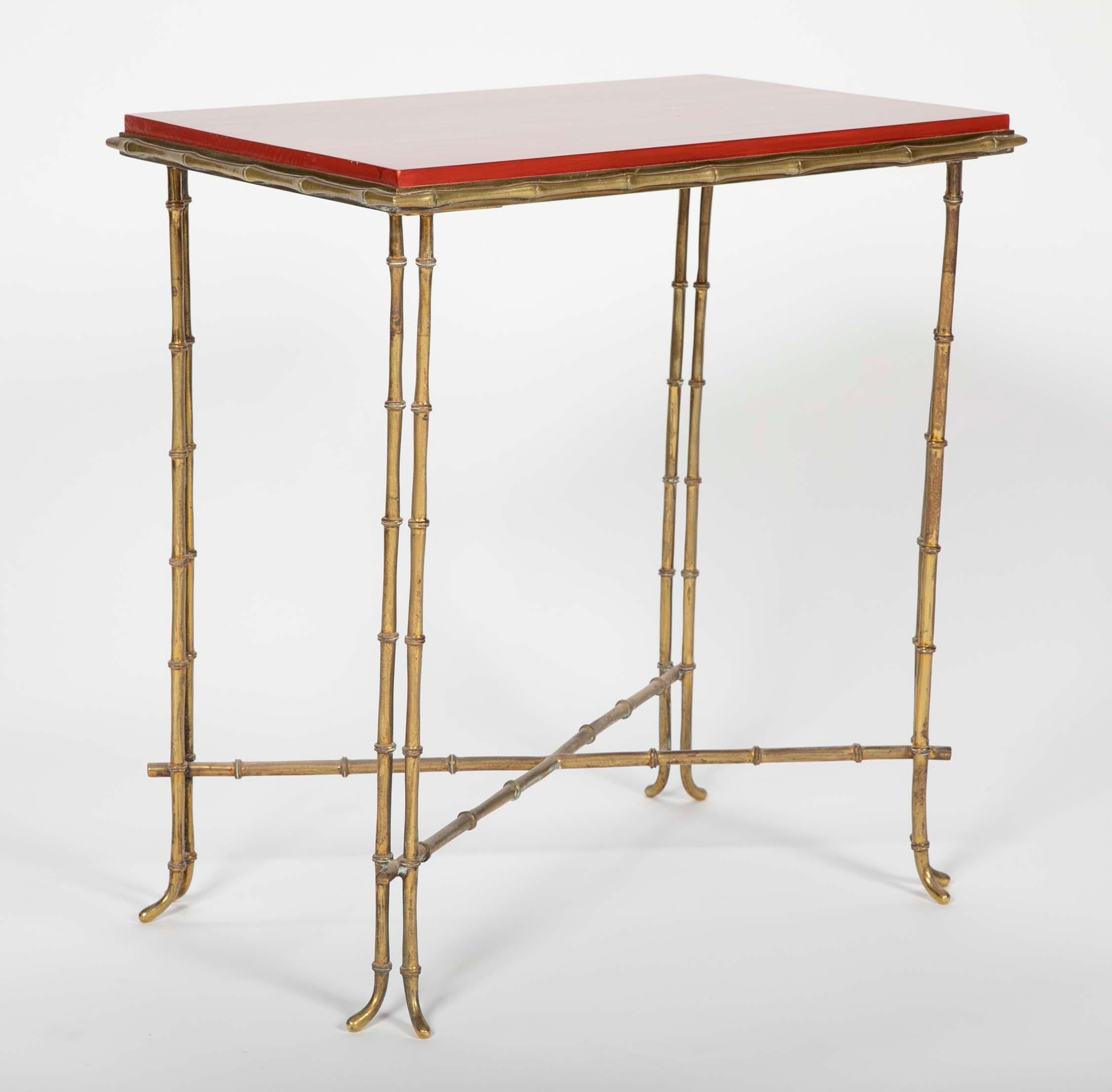 A faux bamboo brass side table rising on four double bamboo form legs with Chinese red lacquered top.