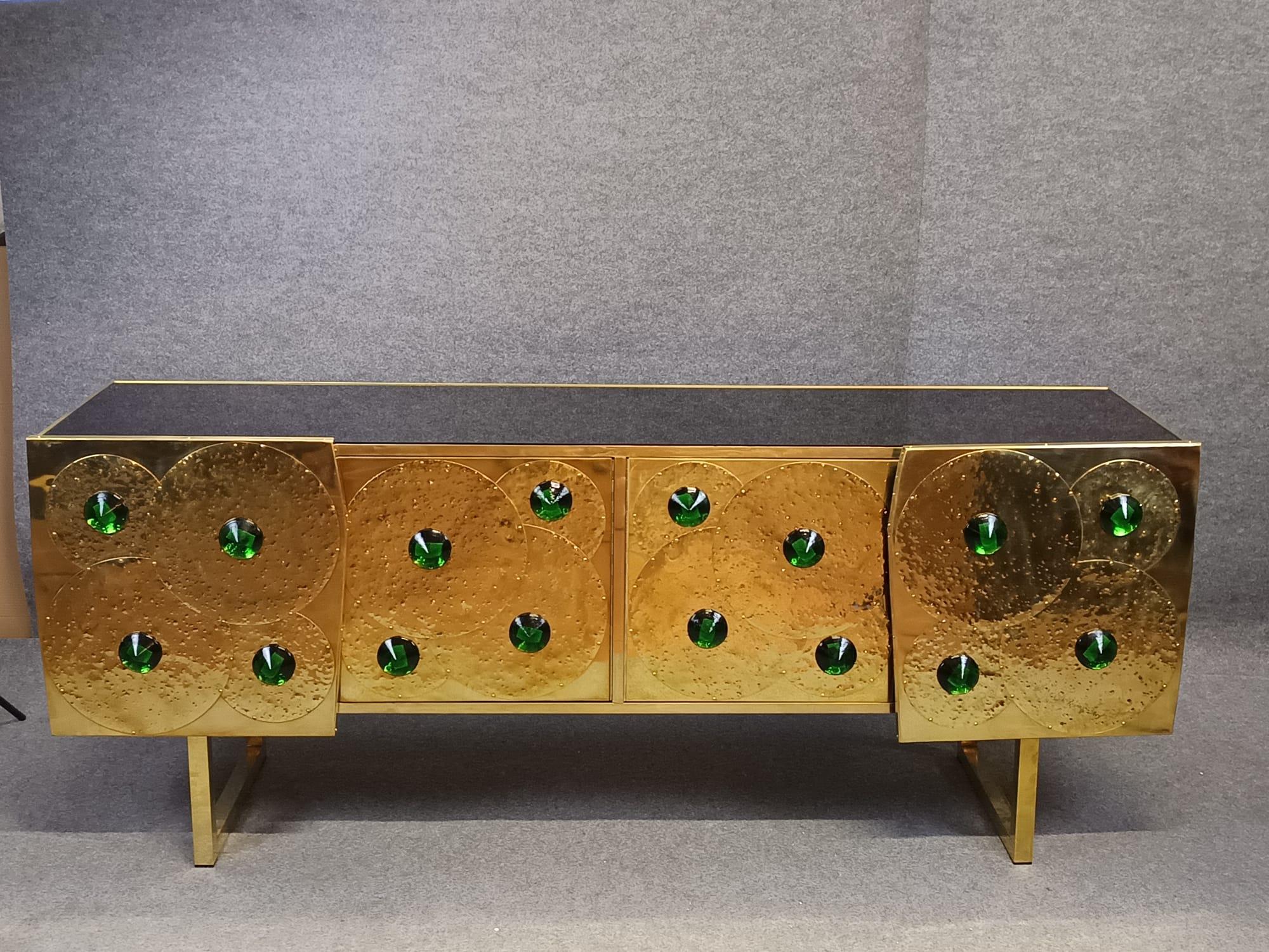Dieses atemberaubende Sideboard aus Messing und schwarzem Glas mit 24 grünen Muranosteinen ist ein Meisterwerk italienischer Handwerkskunst und verkörpert die Eleganz des modernen Designs der Jahrhundertmitte. 

Dieses mit Präzision handgefertigte