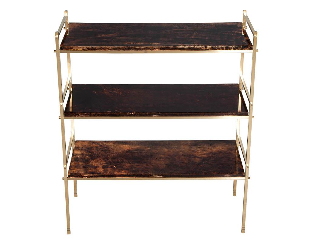 Brass Bookcase Console by Aldo Tura. Crafted in Milano Italy, using goatskin and brass plated frame. Goatskin shelves are lacquered in a high gloss finish. Completed with unique brass plated frame design. This Italian 3 tier 1960’s design can be