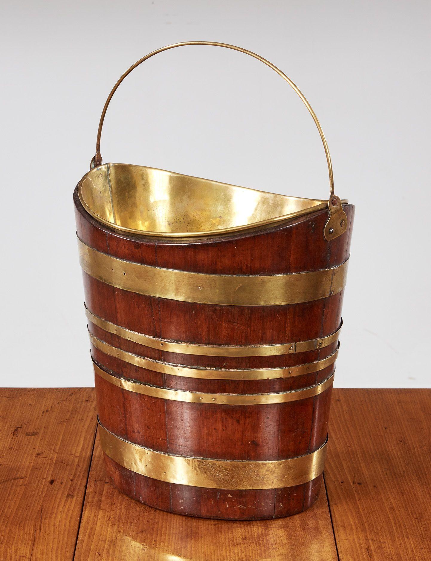 A 19th century boat shaped bucket with coopered mahogany staves bound with two wide and three narrow brass bands, with a brass swing handle, and a removable brass liner.  Strikingly handsome as a fireside kindling bucket or a wastepaper basket.