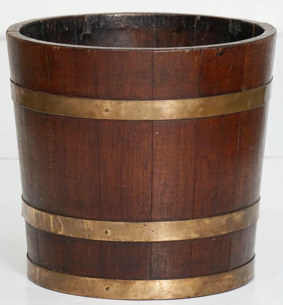 Un fino enfriador o cubo de vino inglés construido con duelas de madera de roble patinado con bandas de latón utilizado originalmente para la presentación de vino y champán pero también atractivo como macetero para flores y plantas.