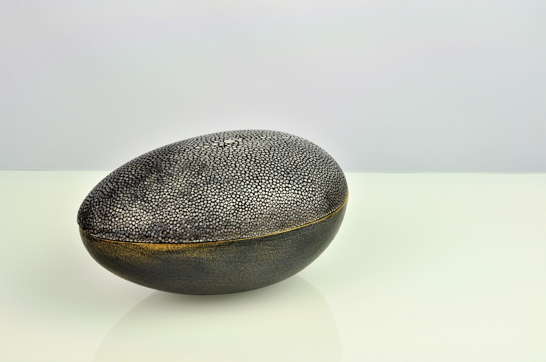 This beautiful organic box is made of brass. The outside has a burnished brass finishing while the interior is polished. 
The lid is made of shagreen. The piece available is in dark grey color (Our ref CARBON).
The underside has a black micro