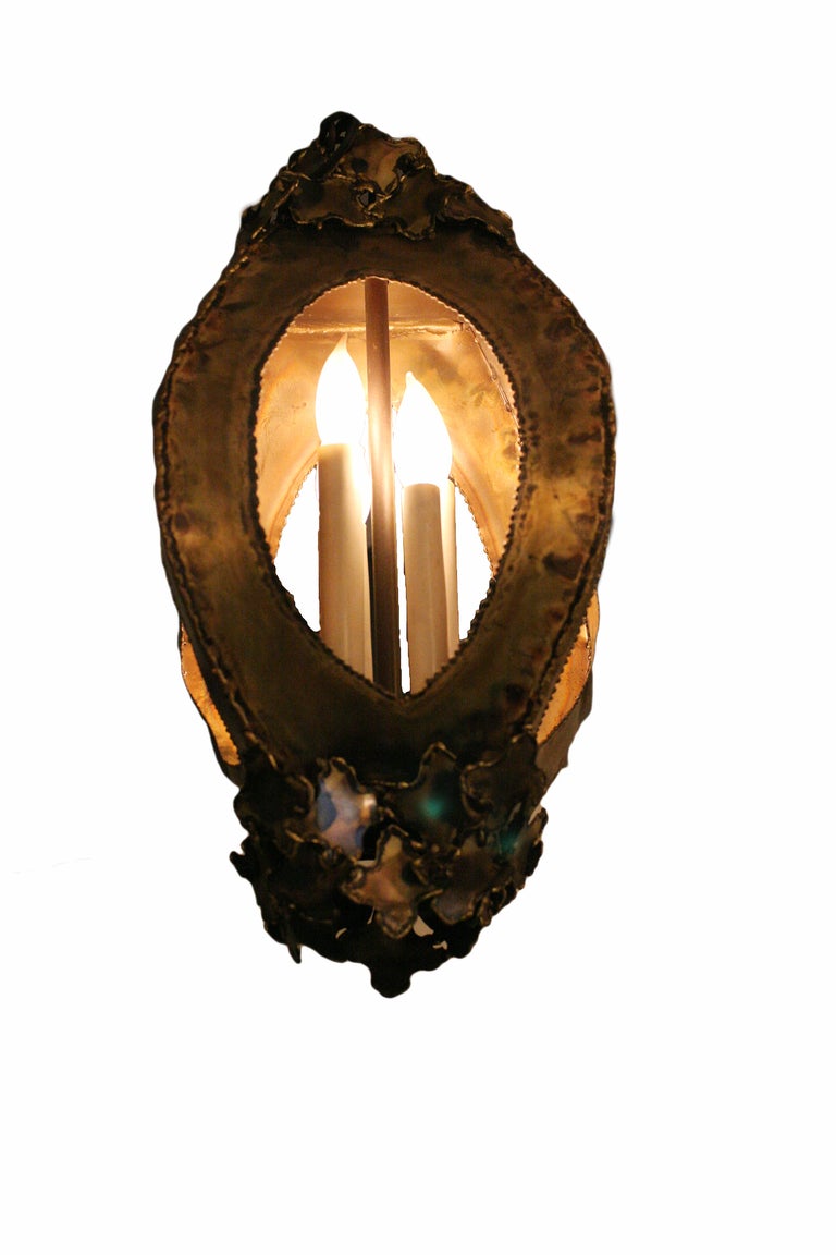 This brass Brutalist pendant in the manner of Curtis Jere is rendered in multiple pieces of layered brass. It features four oval openings which reveal the four lights inside.



 