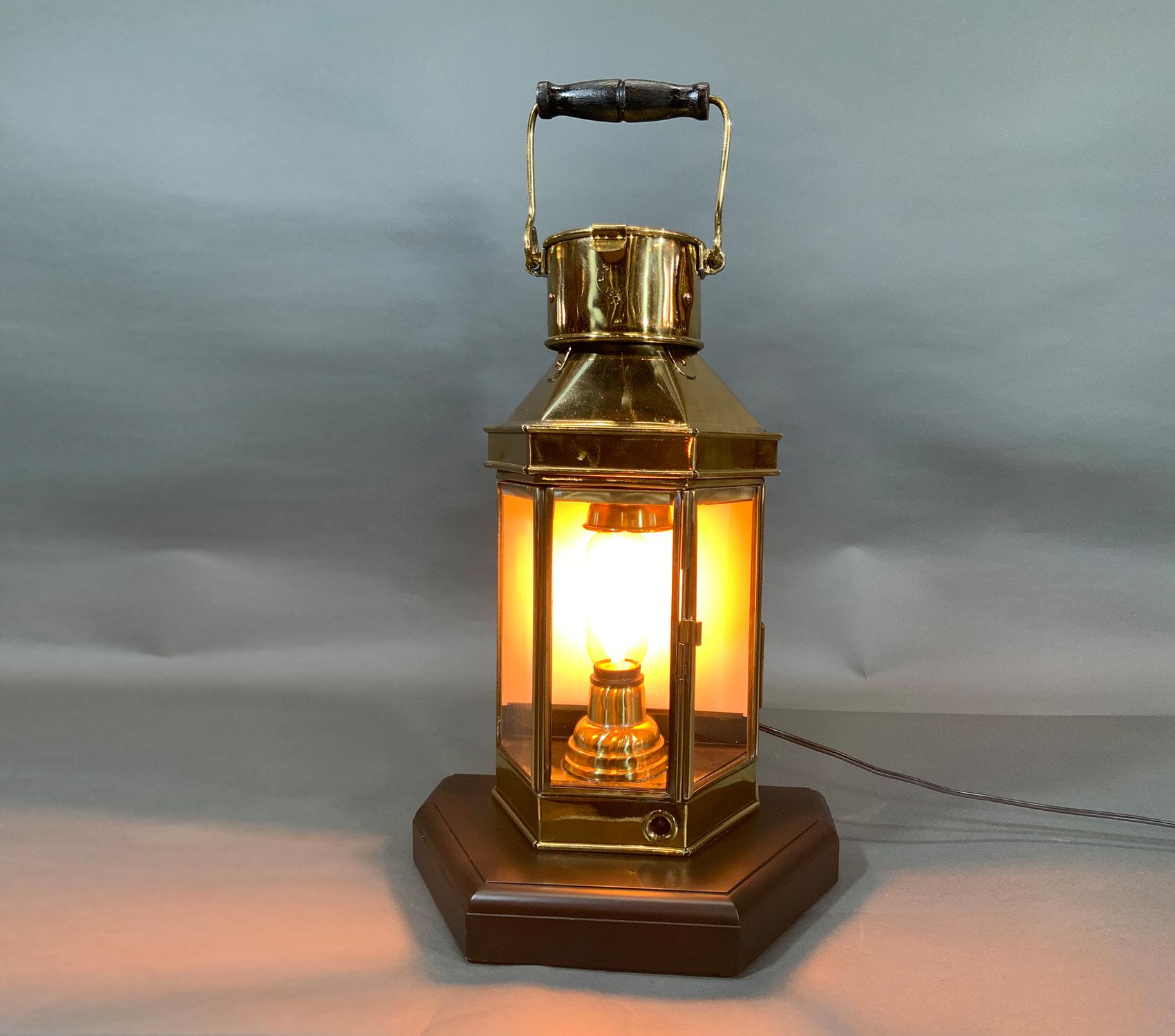 Solid brass ships cabin lantern with highly polished and lacquered finish. With hinged door. Electric socket fit to original burner location for home use with Edison bulb. Mounted to a thick mahogany base. Dated 1942 on top neck.

Weight: 13