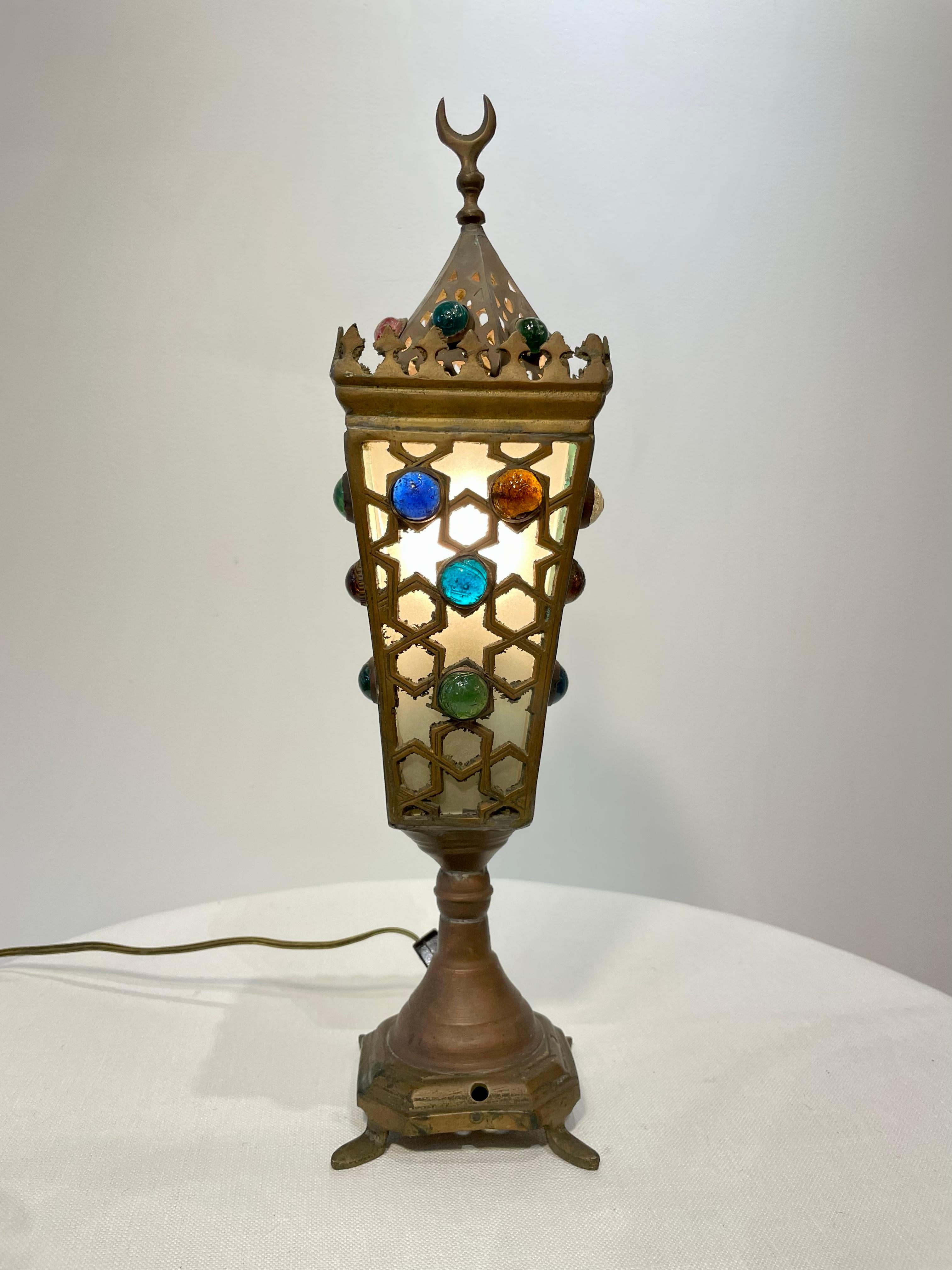 Brass and opaque glass Moorish style small table lamp with covered glass cabochon details. A pierced fret work design covers the glass on all four sides creating a Morrocan pattern in shadow to emanate from the lamp when lit.