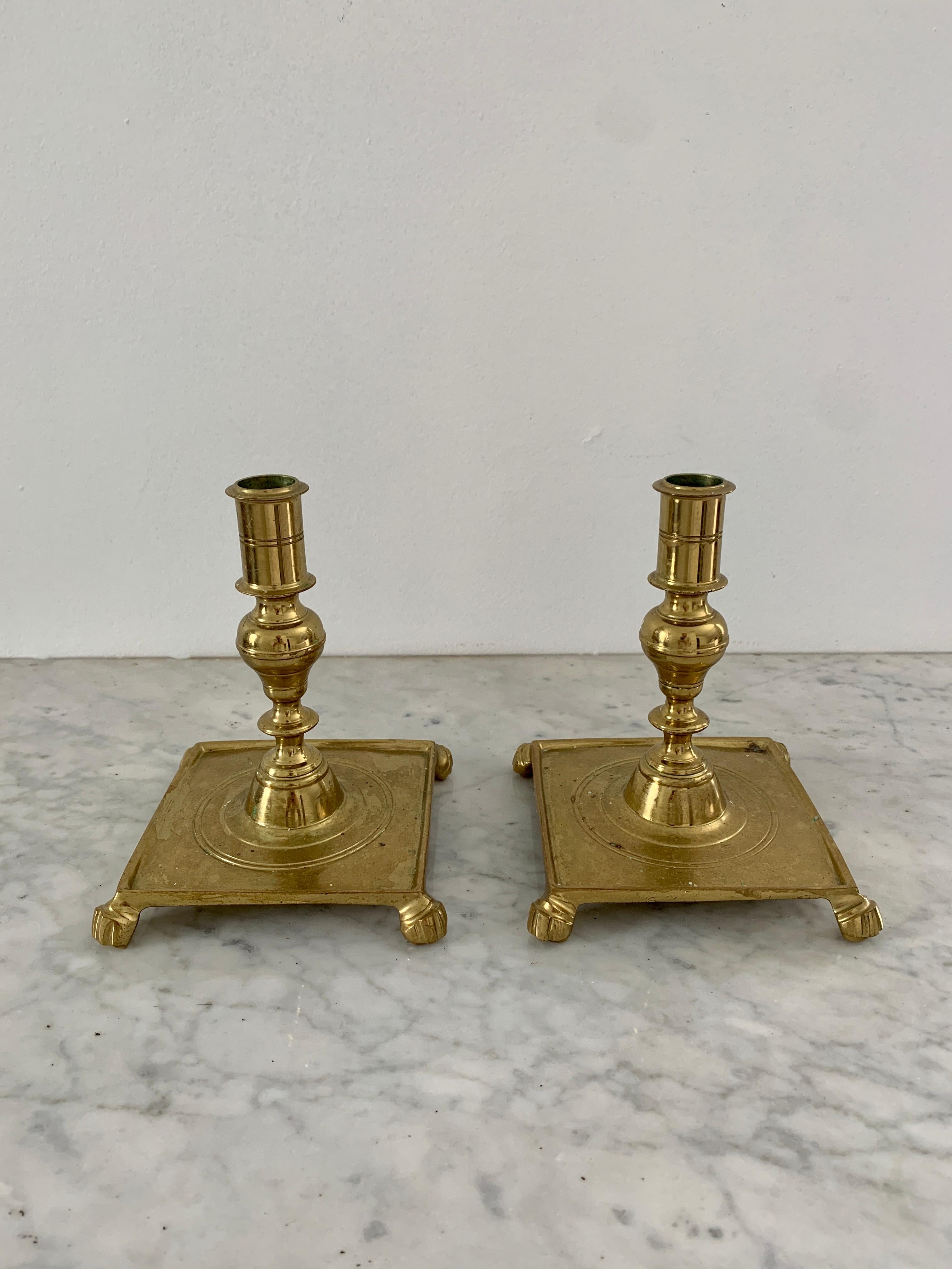 Pair of heavy vintage brass candlesticks on square bases with paw feet. Made by Colonial Williamsburg. This is a 20th century reproduction of a 17th century Spanish style. Measurements are for each.
  