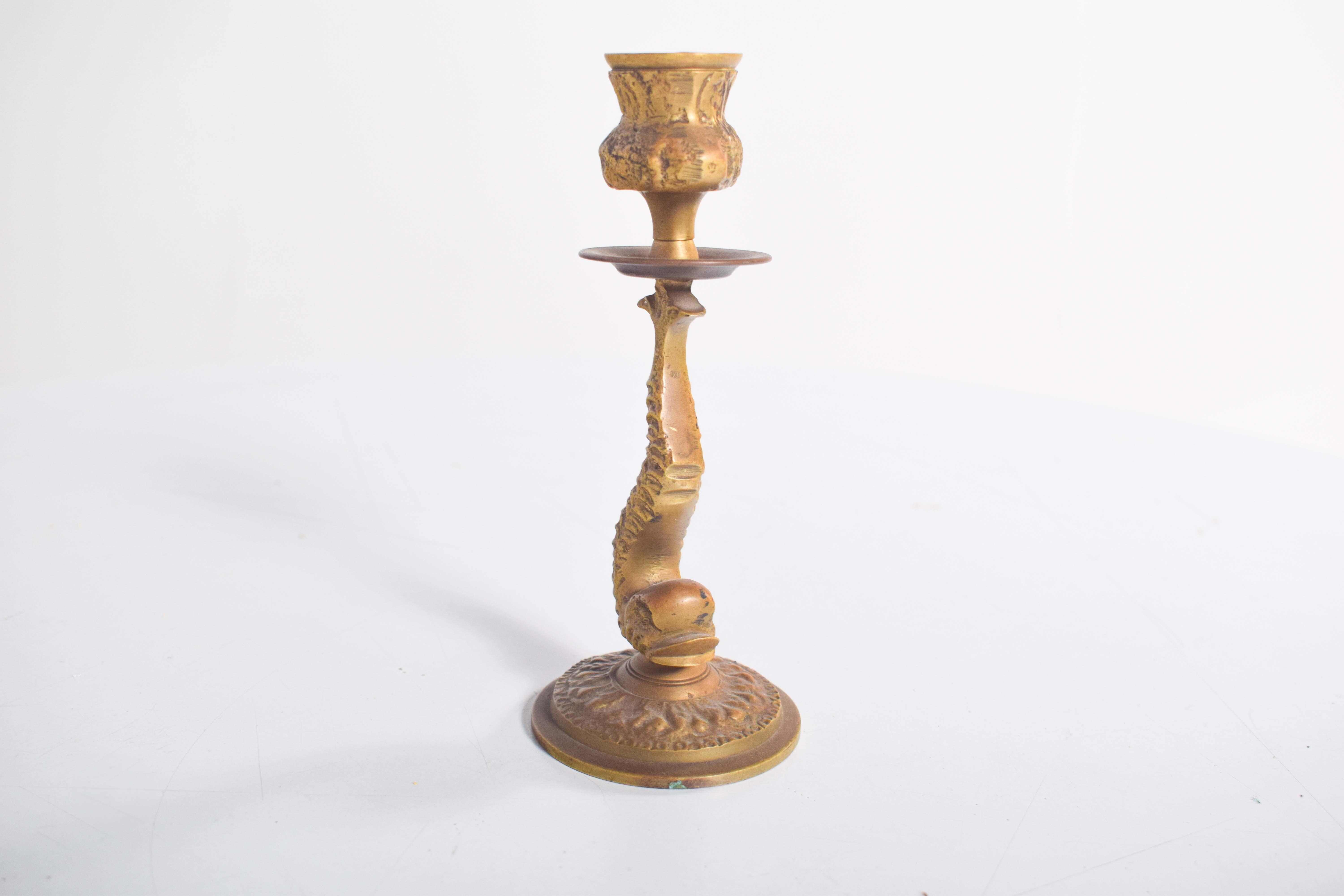 This antique-style brass candlestick features an elegant fish motif, showcasing an intricately detailed design. The fish's head rests gracefully on a round, textured base, while its body curves upward, transitioning into a raised tail that serves as