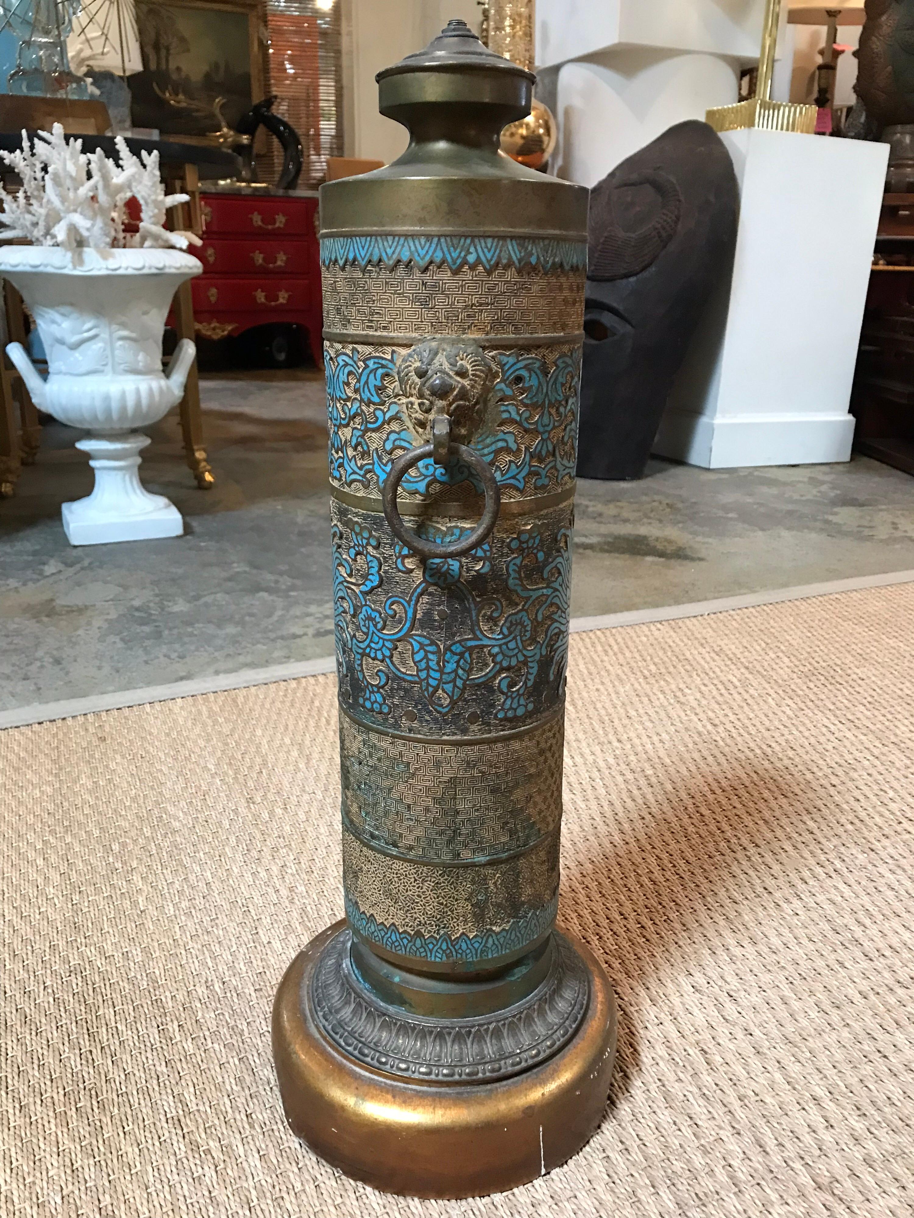 This ornate brass lamp stands as a single column with raised and lowered layers of patterns to decorate the outside. It's turquoise pattern adds a wonderful pop of color to the aesthetic. In need of new wiring.