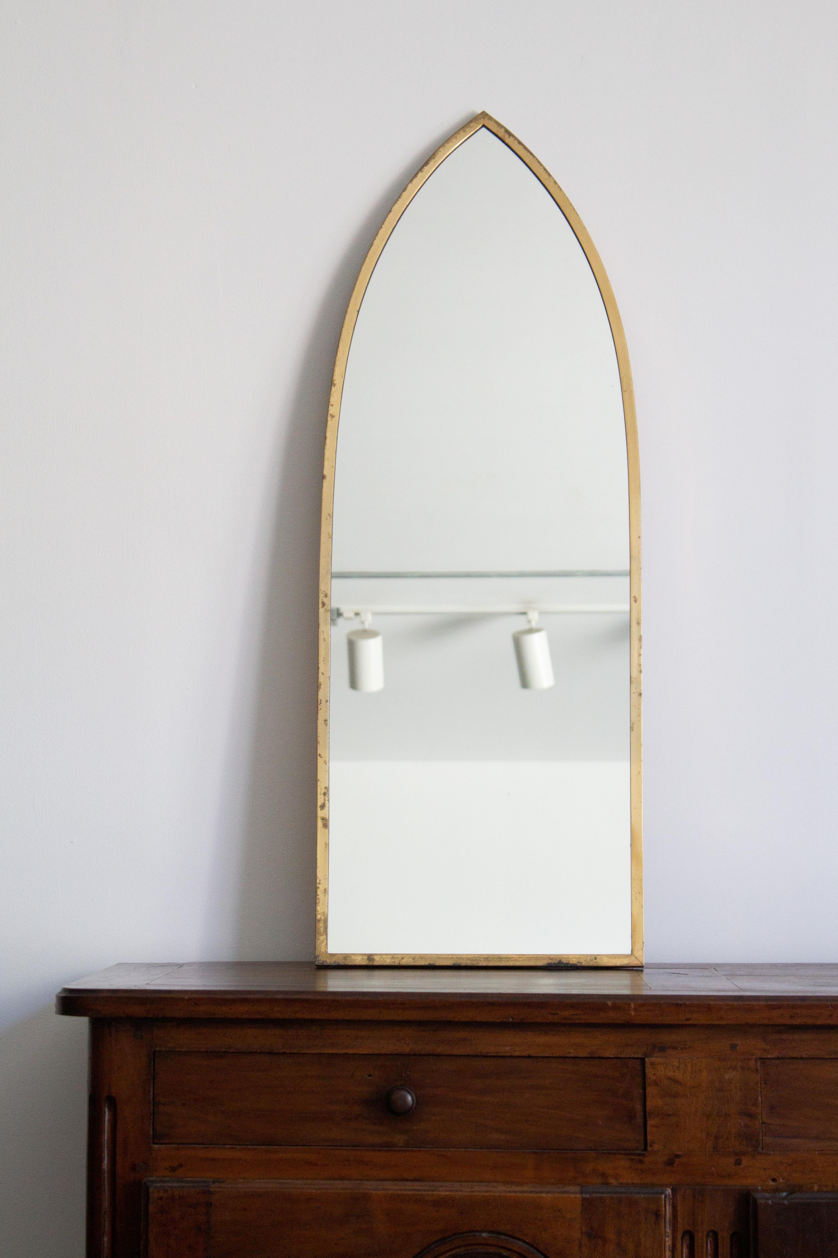 An Italian brass framed mirror circa 1950s. Cathedral arch silhouette. Tarnished patina to brass frame. In the manner of Gio Ponti.