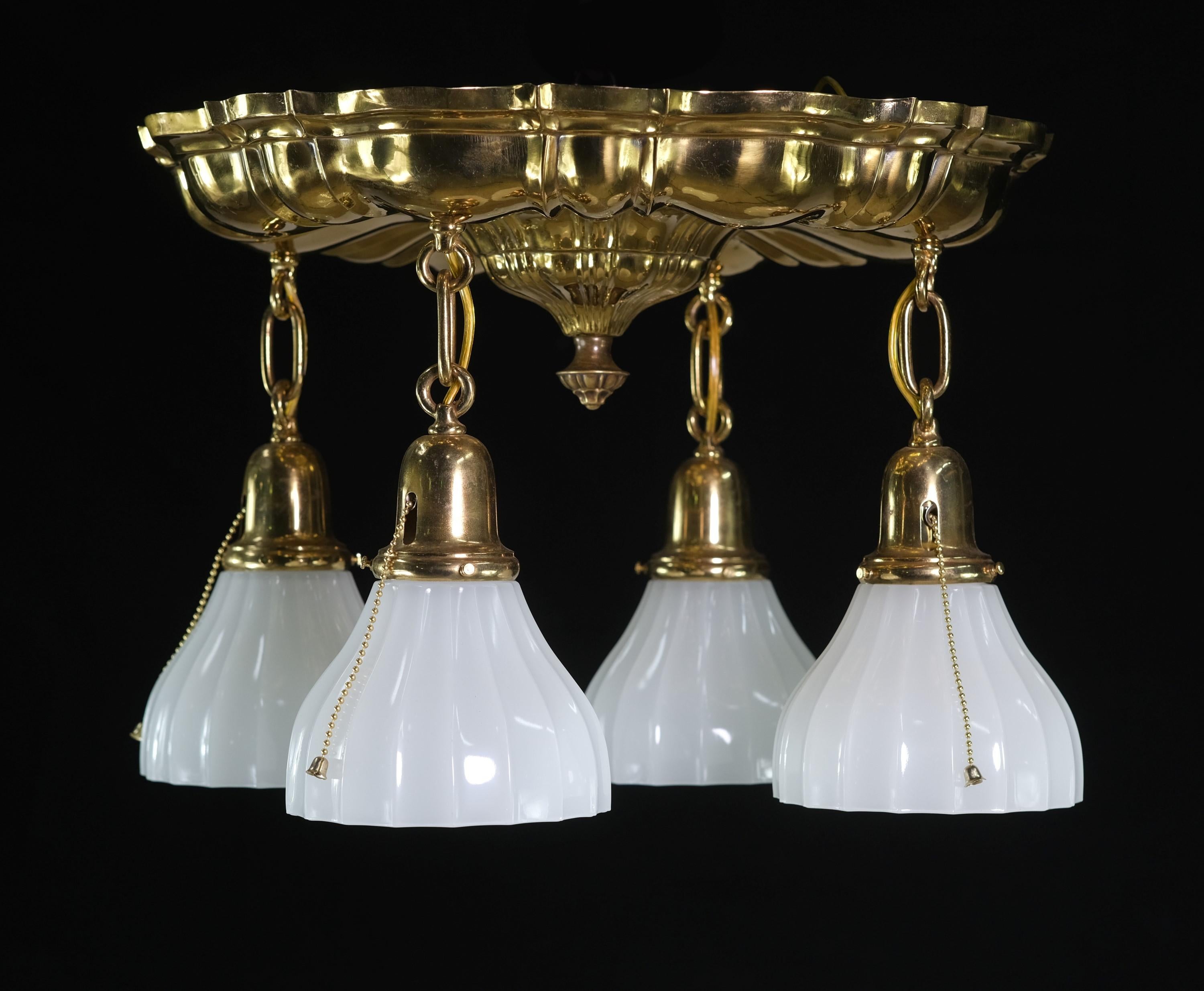 1910s polished brass ceiling mount pan light fixture pendant featuring four hanging down lights. Original milk glass shades. Minor chipping along the edges of some shades. Attributed to Sheffield Lighting. This can be seen at our 400 Gilligan St