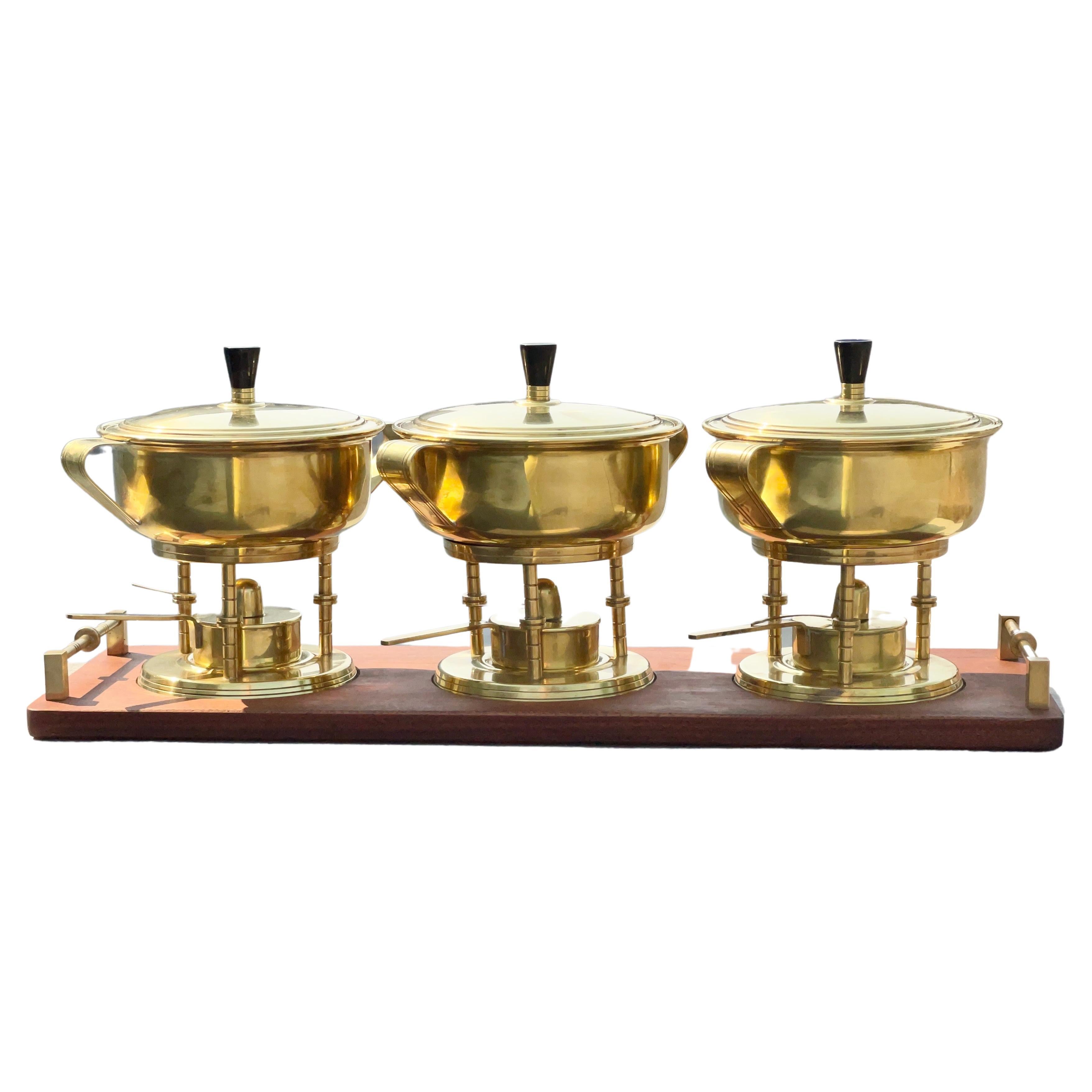 Tommi Parzinger designed set of three lidded solid brass chafing dishes (including Pyrex glass inner bowls) on food warmer stands with handled vessels for fuel oil and cotton wick together with snuffer. Bakelite handles on lids. All standing in a