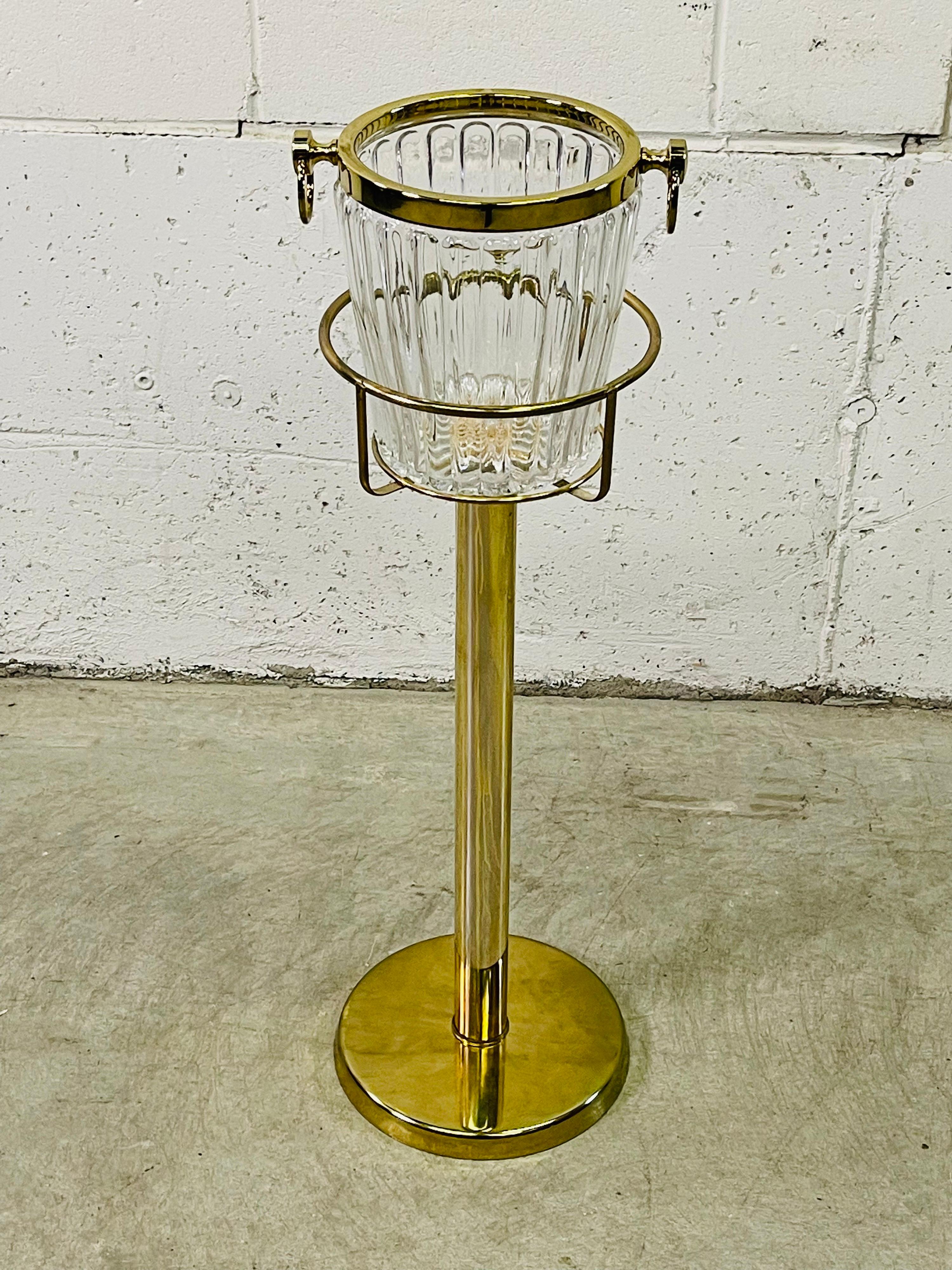 Vintage 1970s champagne glass ice bucket with brass stand. The ice bucket has a brass rim and handles. The stand has a heavy base and sturdy. No marks. Ice bucket measures: 7.5” diameter x 8.5” height.