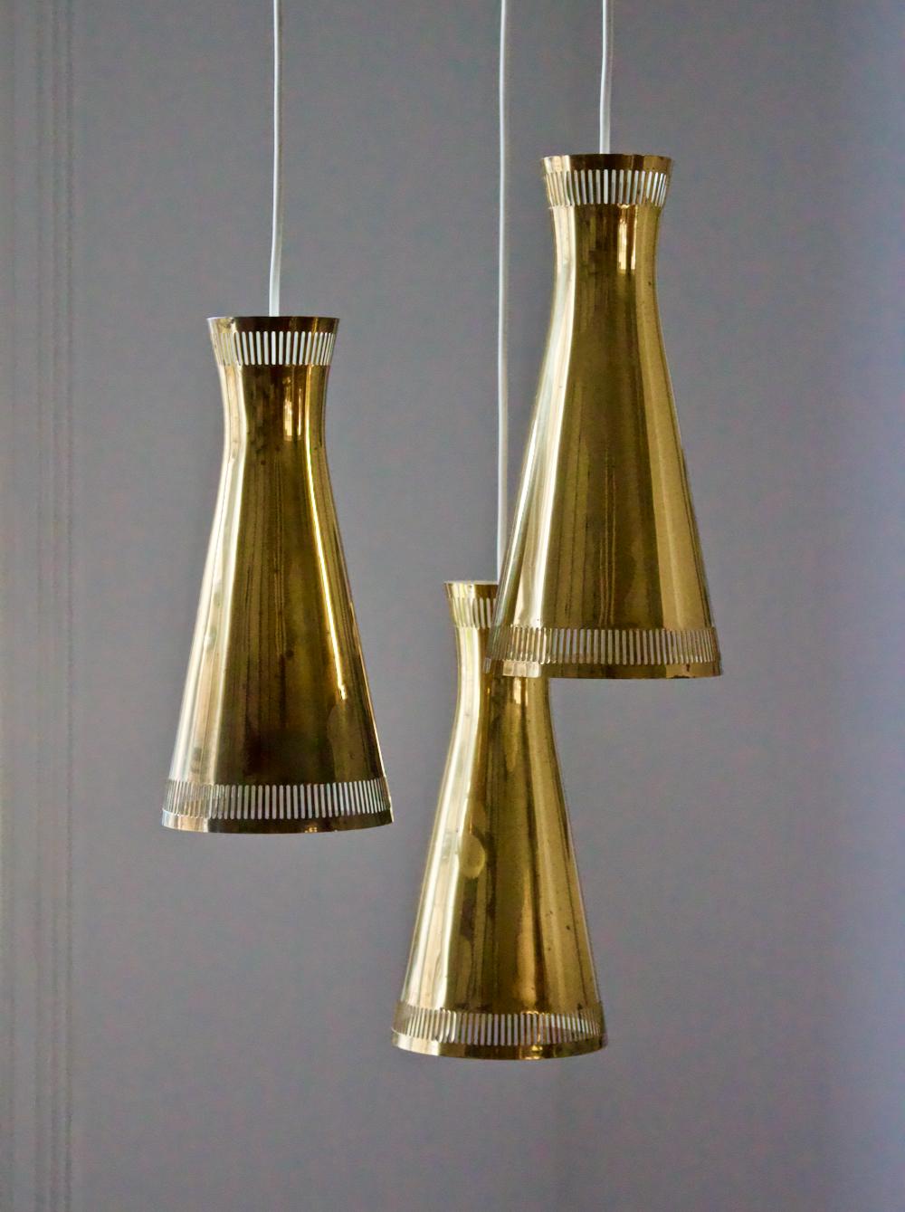 Brass chandelier, for Itsu, Finland. Mid-20th century.

A high-quality cascading chandelier featuring three shades of polished brass - white on the inside - arranged at different heights. The original ceiling canopy is in place and the fixture has