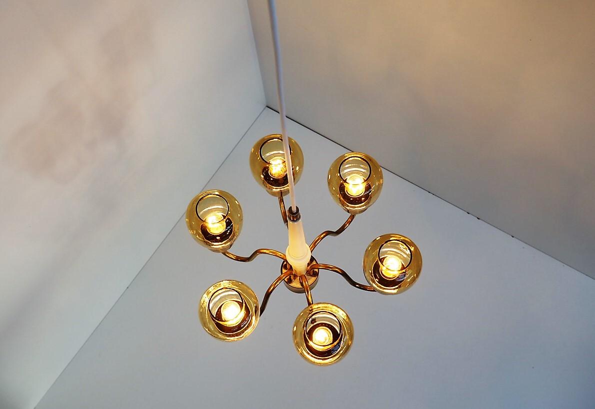 Six armed brass chandelier with amber colored glass shades and white centre rod made in wood. The light is designed by Hans Agne Jakobsson in the 1960s and the model has number T-526.
It´s manufactured by Hans Agne Jakobsson A/S Markaryd in Sweden