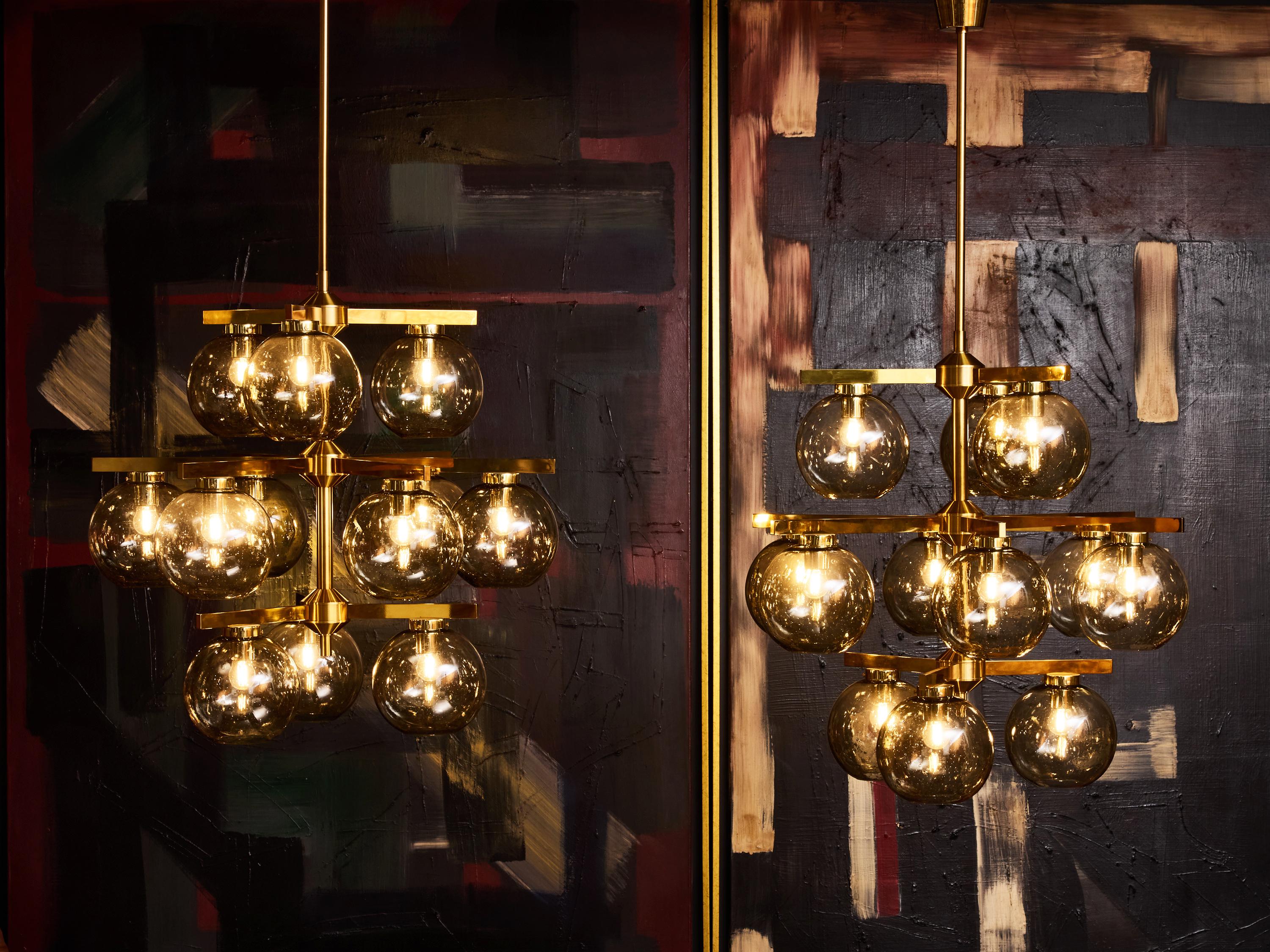 Remarquable et sculptural, ce lustre Westal présente un design dramatique composé de globes en verre fumé montés sur un cadre en laiton poli. La structure à plusieurs niveaux crée une silhouette dynamique, tandis que les globes régulièrement espacés