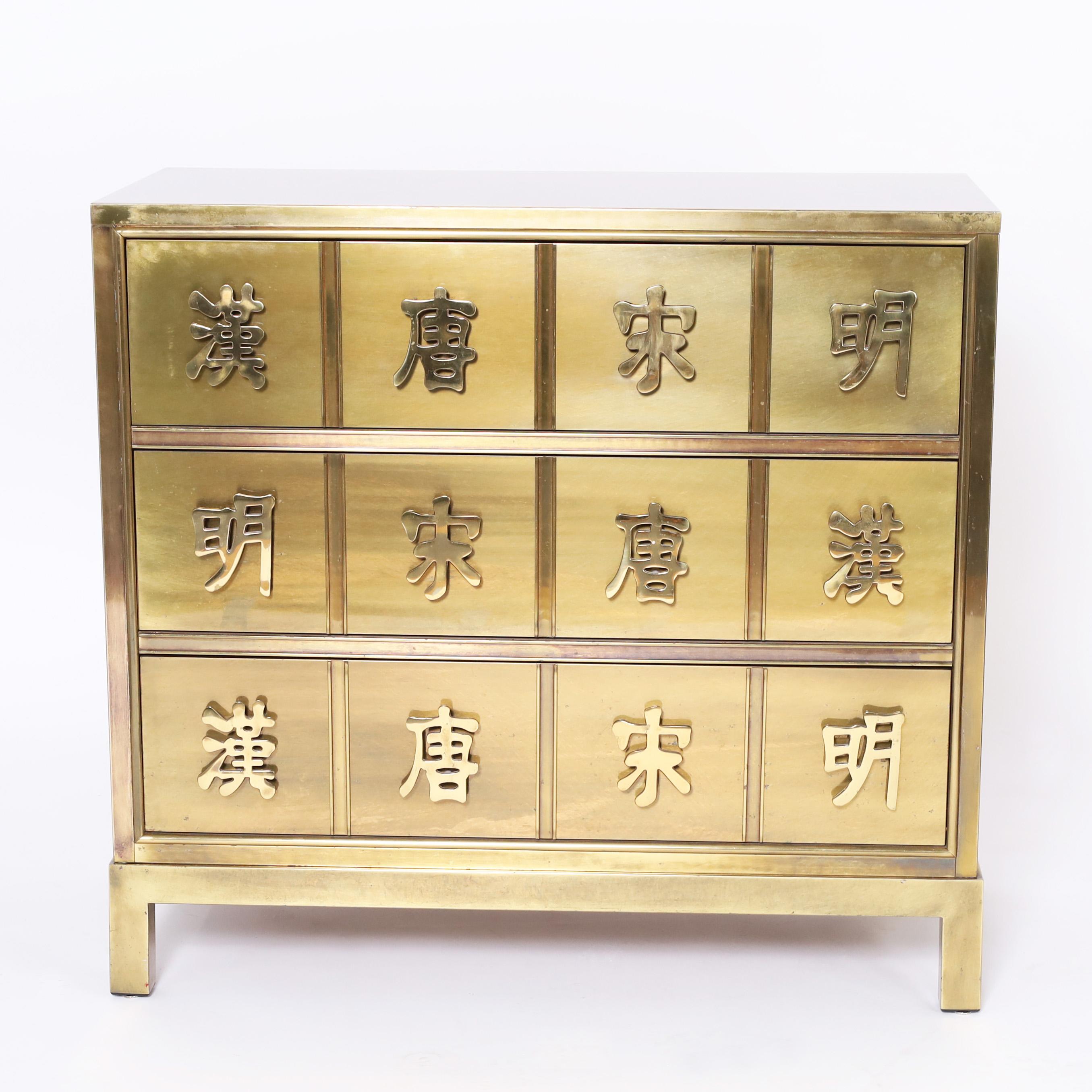 Chic mid century chest of three drawers crafted in a sleek modern form entirely clad in brass with a hip acid washed finish featuring Chinese characters as drawer pulls signifying the four dynasties. 