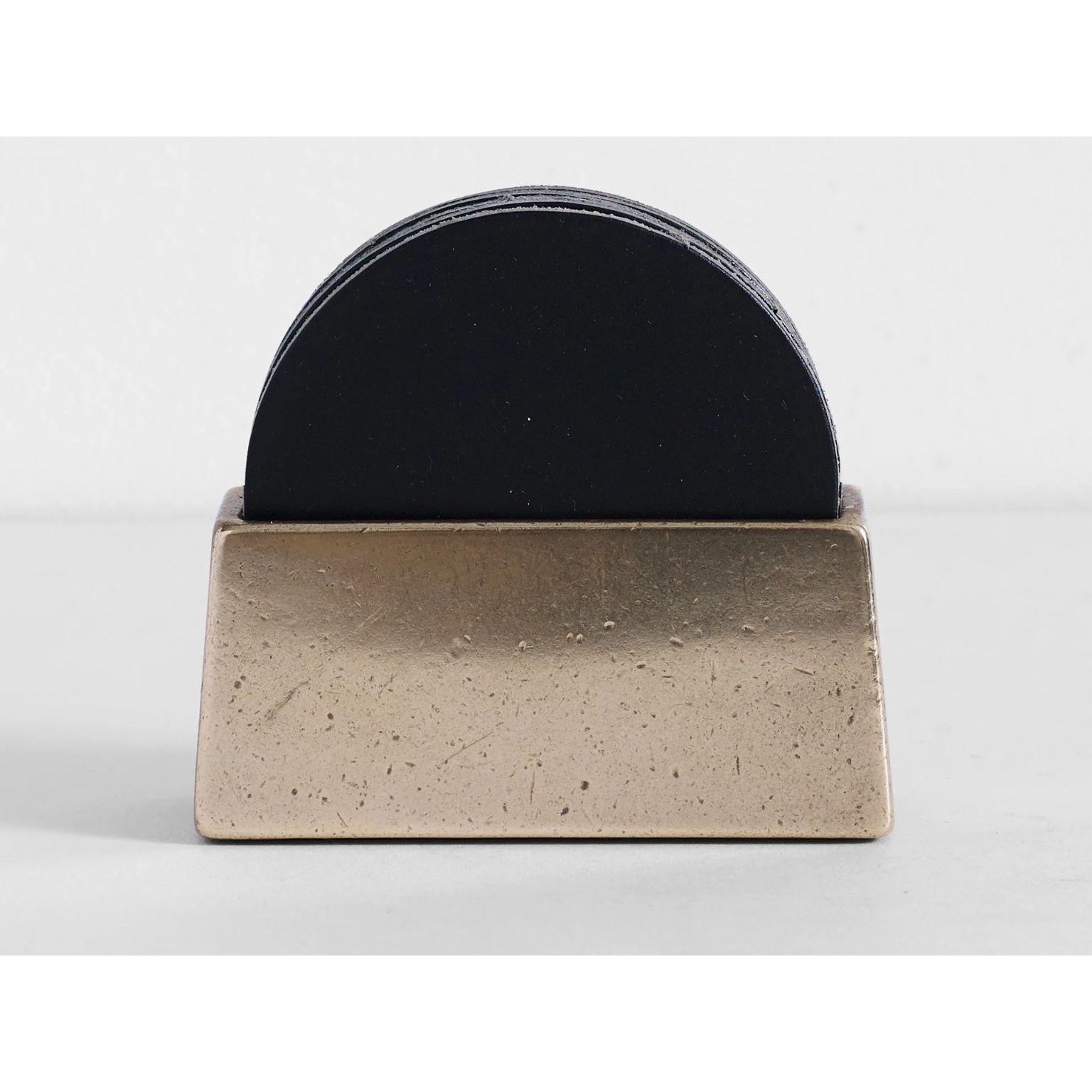 Brass Coaster Holder With Black Coaster Set by Henry Wilson
Dimensions: D 4 x W 4.8 x H 10.5 cm
Materials: Solid brass, Leather

Sand cast in solid brass and hand finished.
Holds 6 Tan leather coasters that are included with holder. 
They are