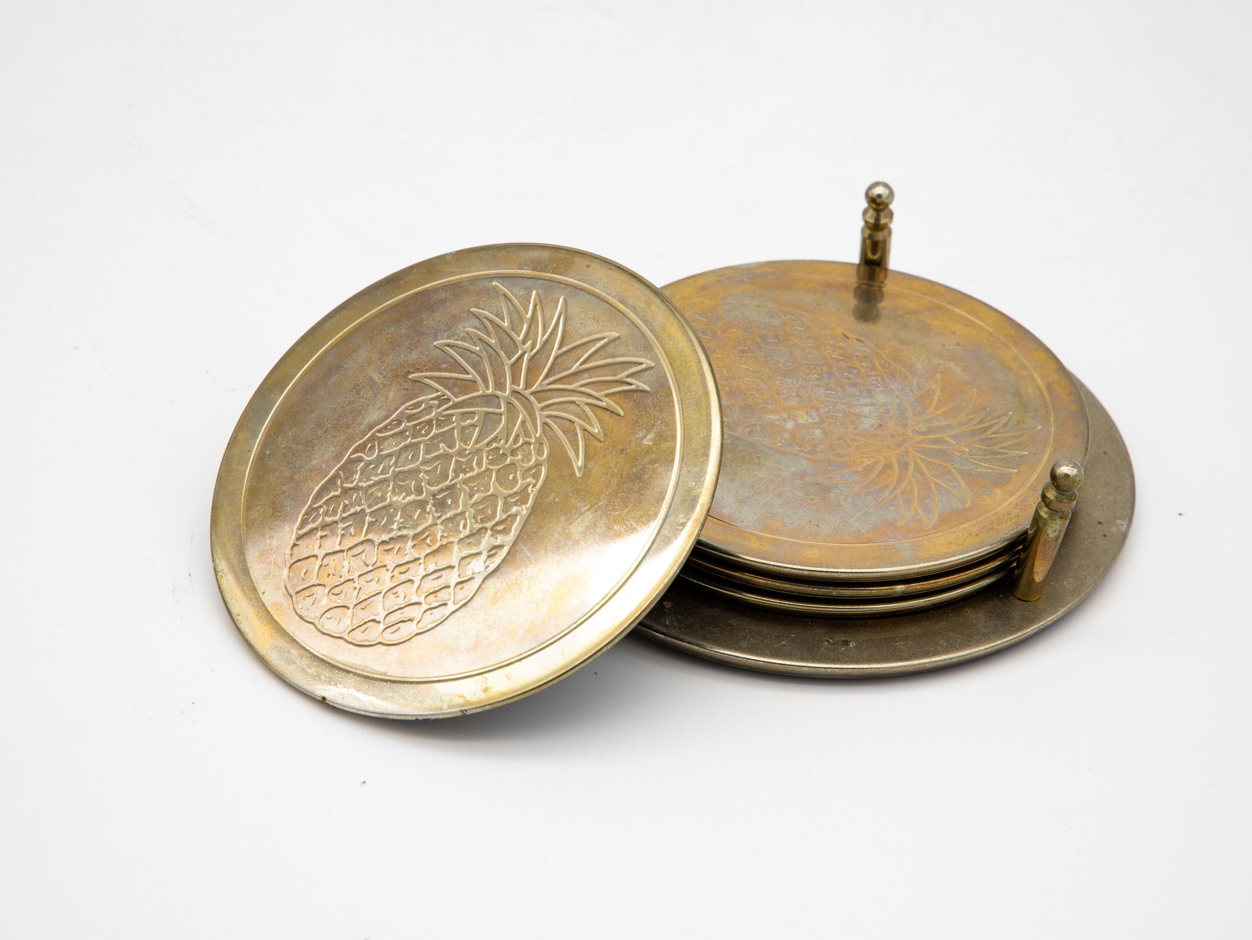 A set of five brass coasters with a holder. Each coaster has a pineapple etched in the top. Ample patina for the true vintage lover.