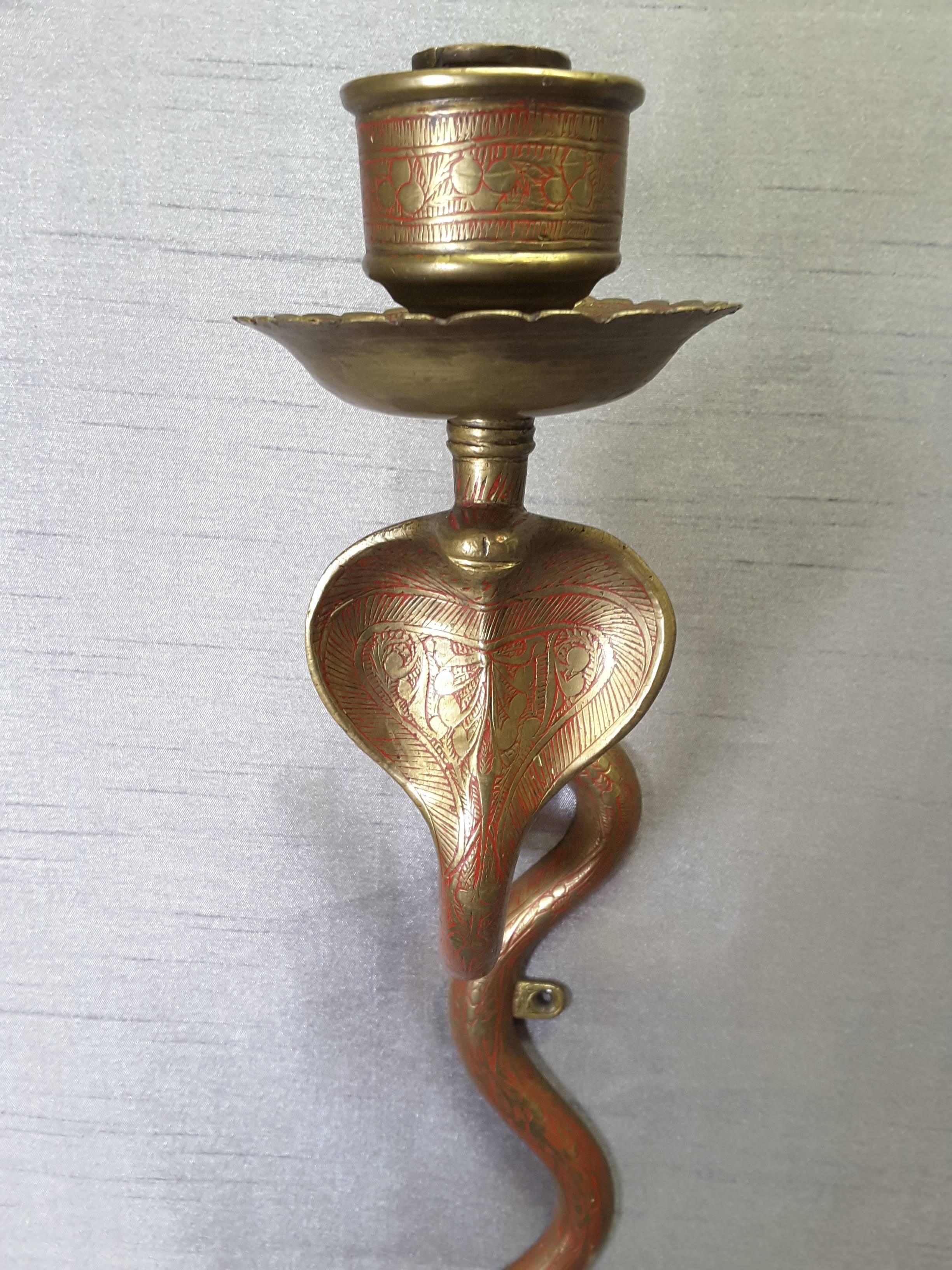 A Single Brass Cobra Sconce engraved decoration with red detailing, circa 1960s. The sconce has a single candle cup holder with drip cup, Open hooded cobra with S-shaped body, with two mounting brackets for screws. The sconce measures 20