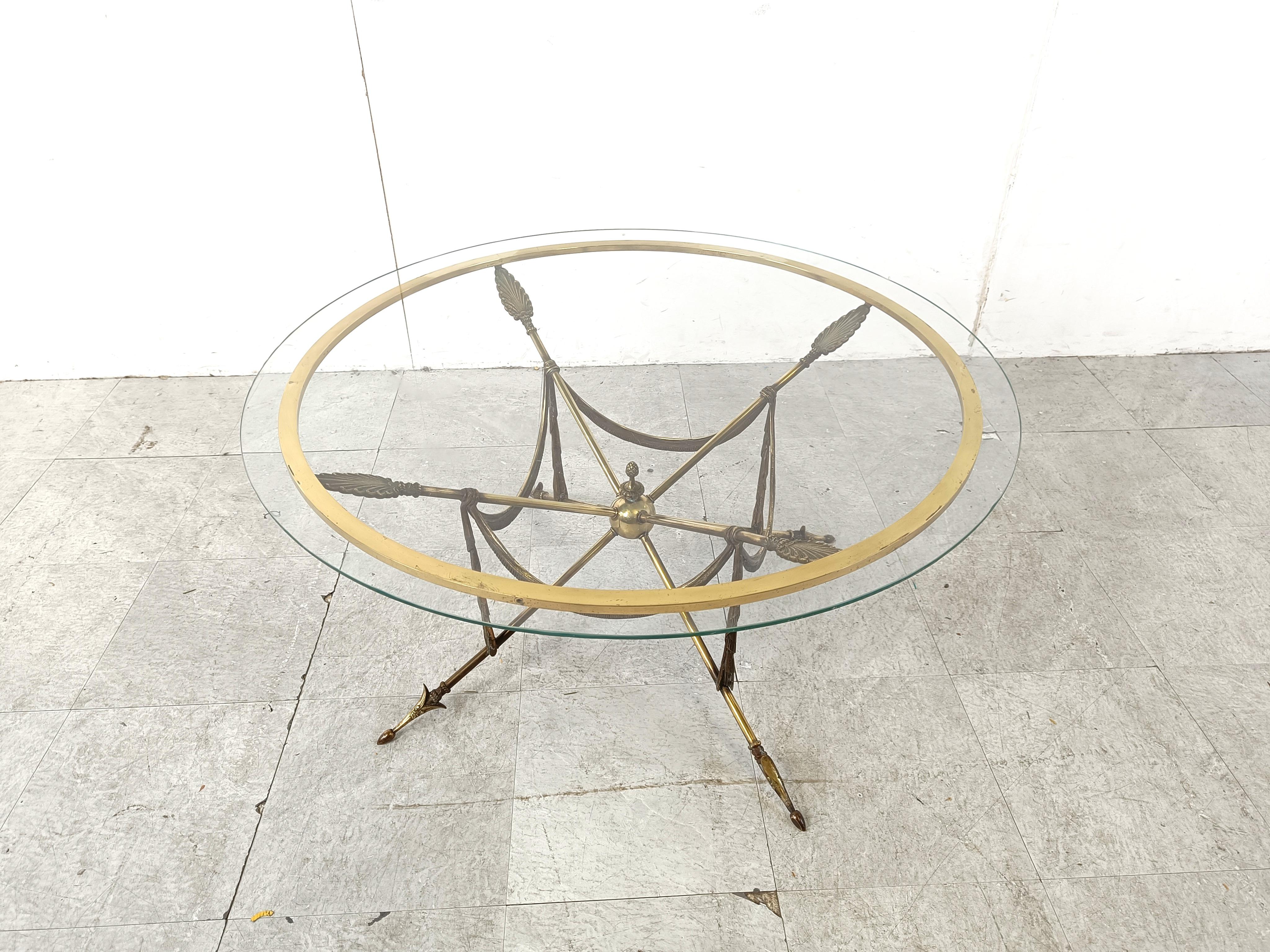 Striking vintage coffee table with brass arrows and tassel shapes with a clear glass top.

Very much in the style of Maison Jansen.

Beautiful neoclassical coffee table made of high quality brass.

1970s - France

Dimensions:
Height: 45cm
Width: