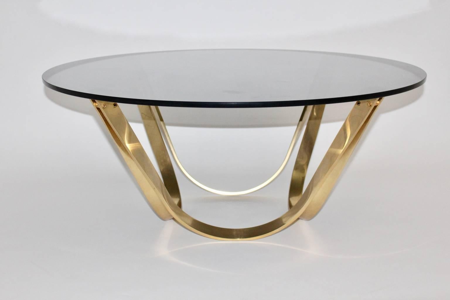 Mid Century Modern vintage coffee table or sofa table circular like from brassed metal and smoked glass top 1960s.
The sophisticated and elegant sofa table or coffee table in brassed metal with beautiful patina features a slightly curved base with a