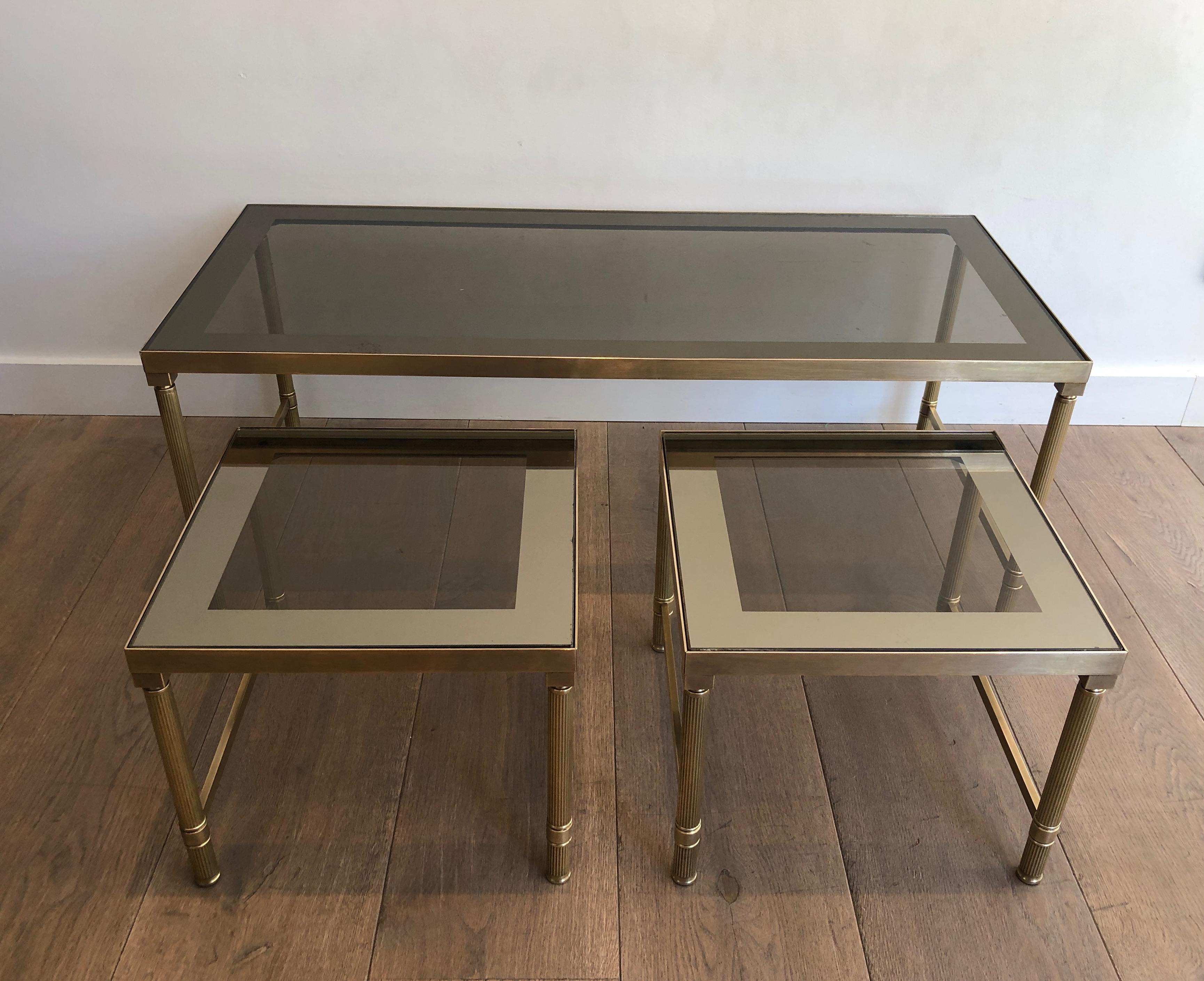 This coffee table is made of brass with glass tops. It is composed of 2 nesting tables that can be used as side tables. This is a French work, circa 1970.
