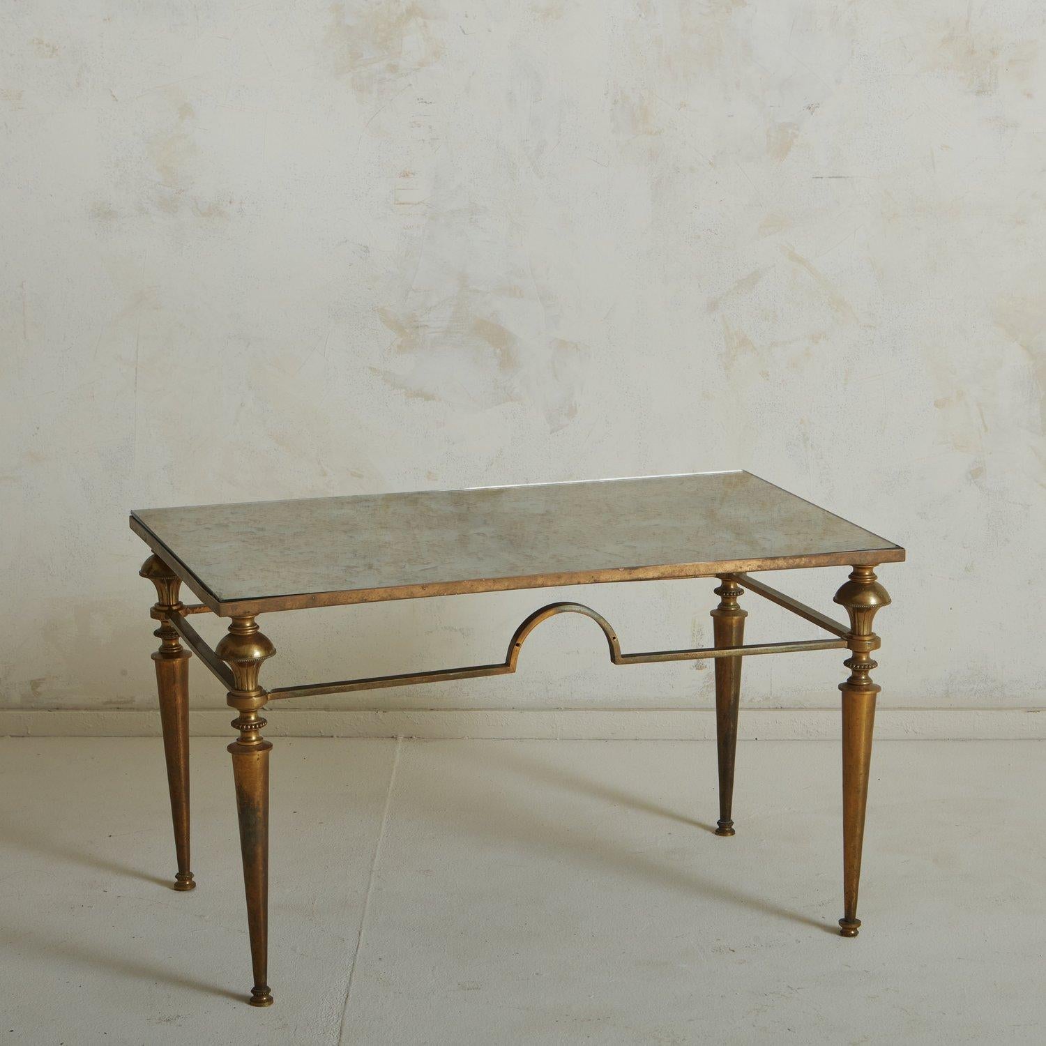 A 1960s French coffee table featuring an intricate patinated brass base with tapered legs and a demilune stretcher detail. It has a beautiful antiqued mirror top. Sourced in France, 1960s. 

