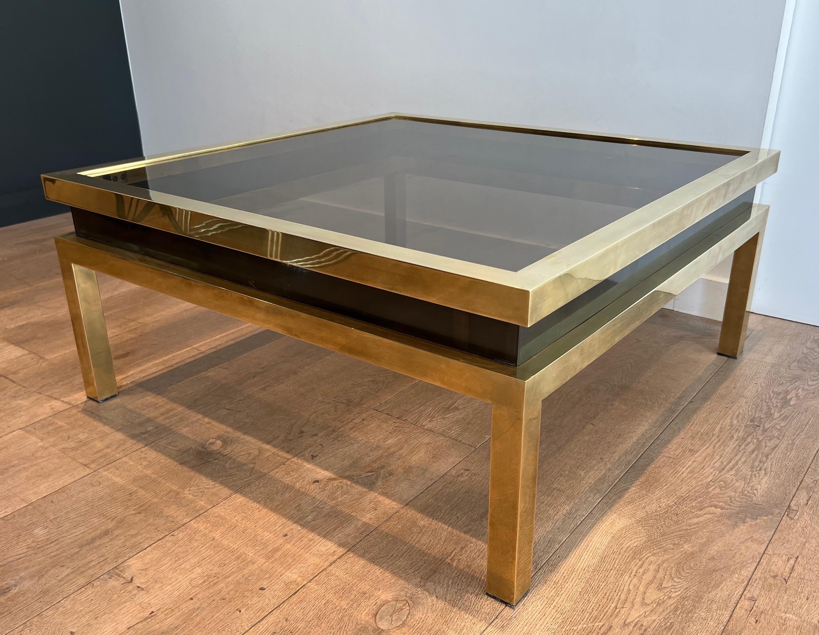 Cette belle et rare table basse carrée est en laiton, entourée d'une ligne laquée noire et surmontée d'une tablette en verre fumé. Il s'agit d'une œuvre française de Guy Lefèvre pour la Maison Jansen. Circa 1970
