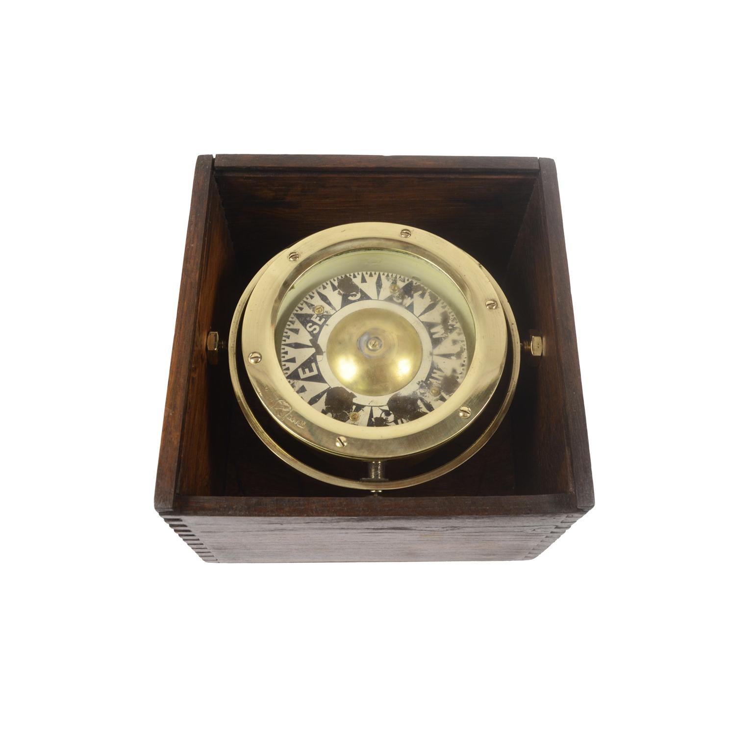 Magnetic compass on universal joint in its original wooden box with slot lid, signed with a trade mark brass emblem engraved with two crossed arrows within a shield, from the end of the 19th century. The compass consists of a cylindrical vessel in