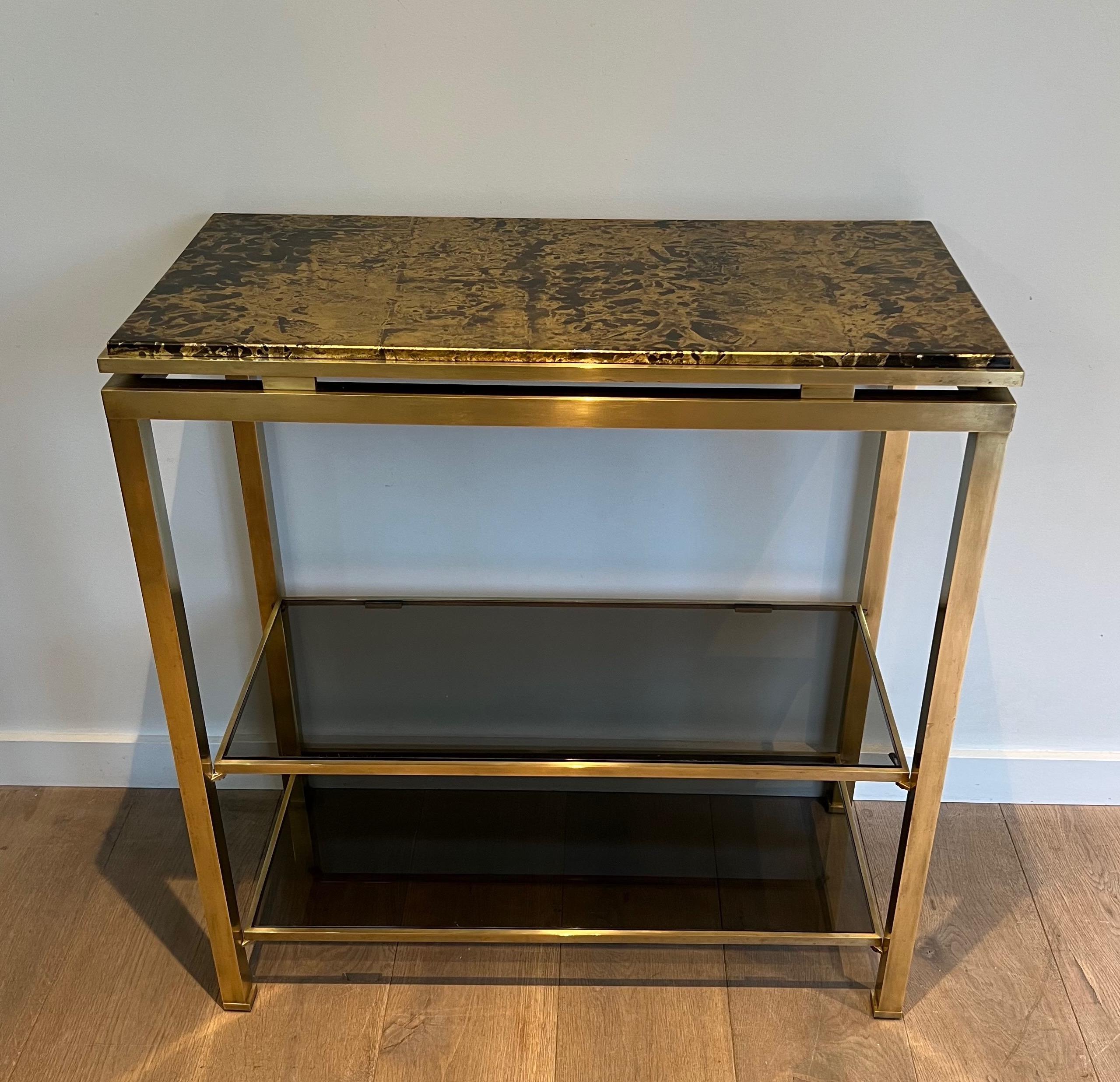 This rare and maybe unique console is made of brass with 2 smoked glass shelves on the bottom part and a gilt top imitating marble. This is a French work by Guy Lefèvre for Maison Jansen. Circa 1970